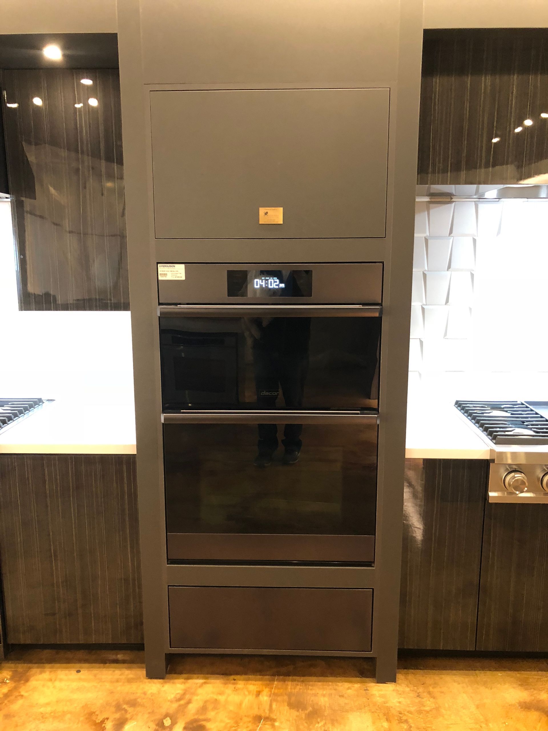 A tall, dark gray built-in oven unit with three compartments in a modern kitchen.