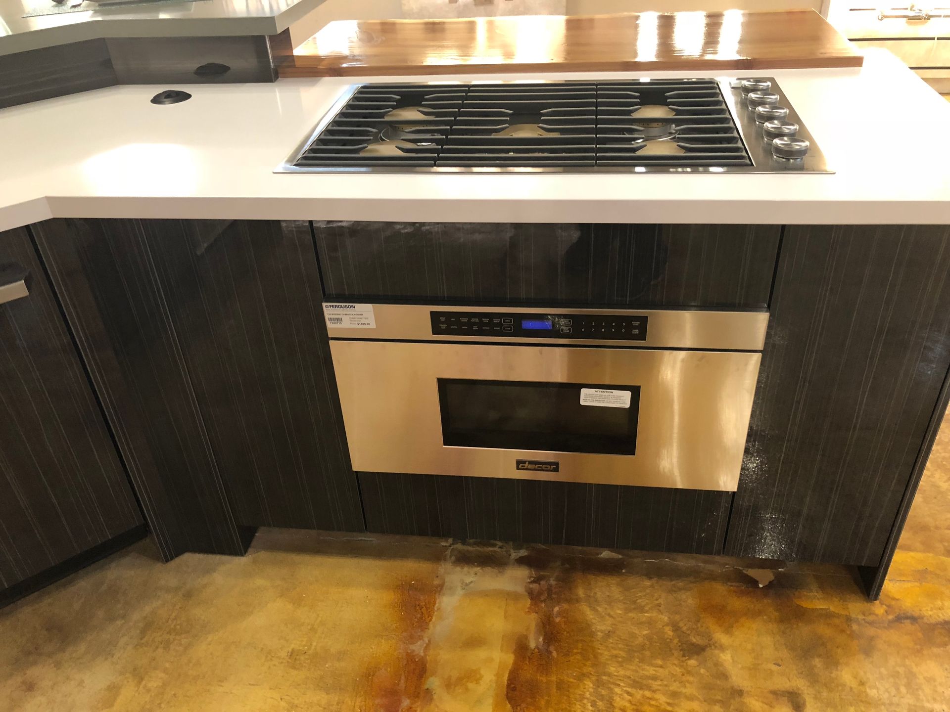 Stainless steel microwave built into a dark wooden cabinet below a stovetop in a kitchen.