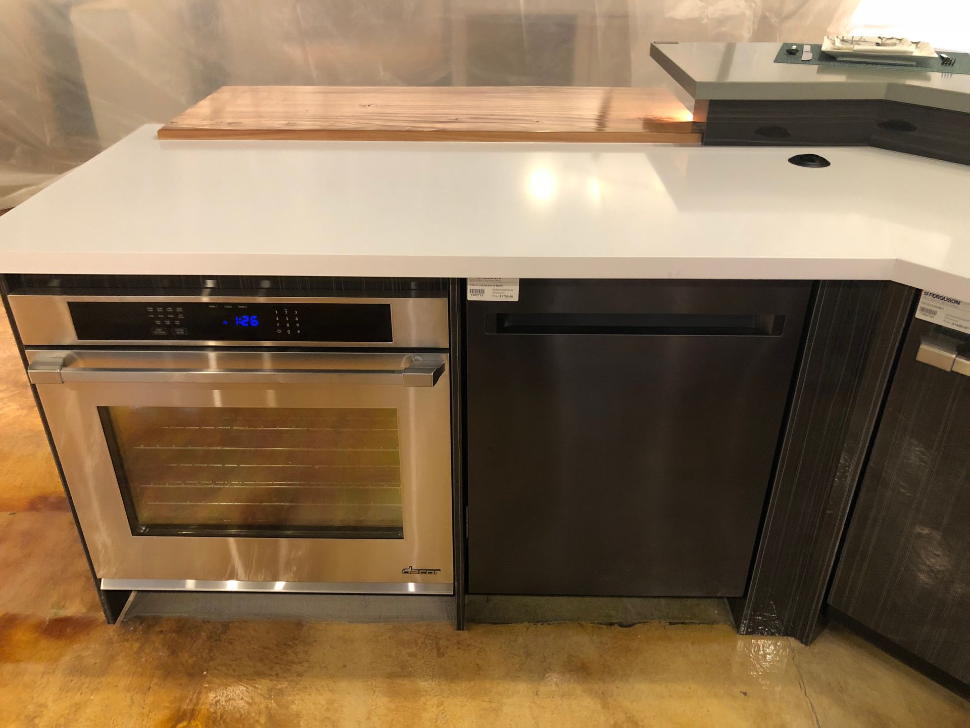 Stainless steel oven and dishwasher built into a white countertop island. Wooden cutting board nearby.