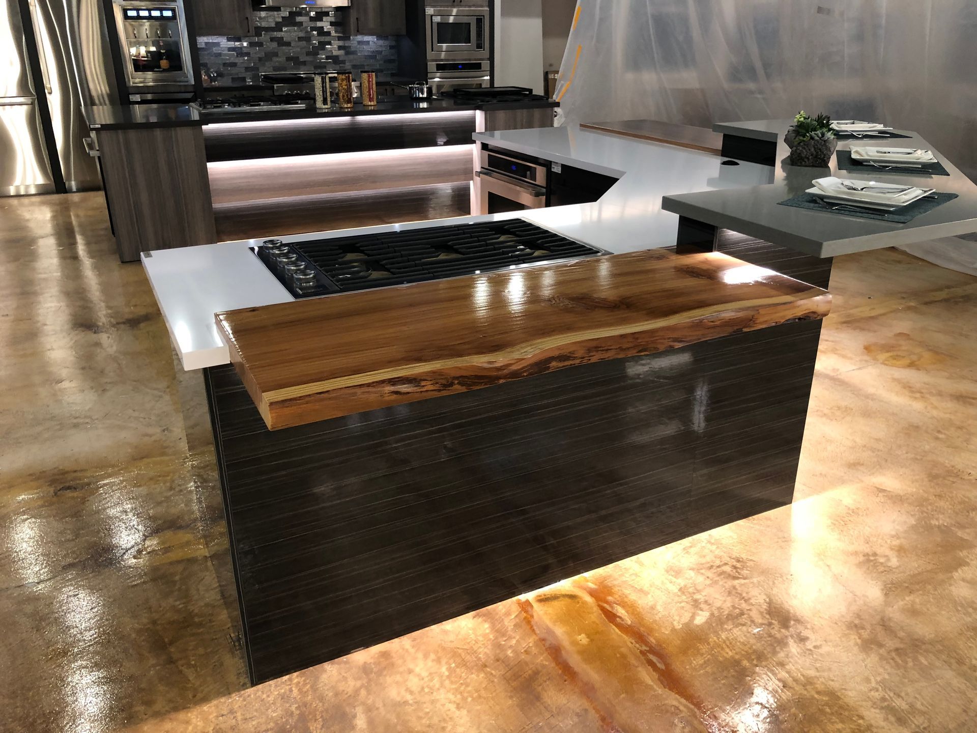 Modern kitchen island with wood and dark countertops. Cooktop, brown, and gray cabinets.