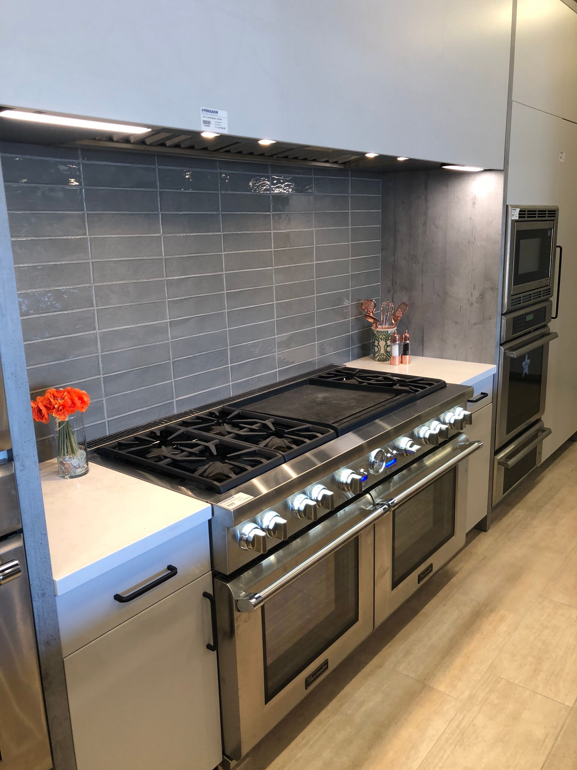 Stainless steel gas range and oven in a modern kitchen with gray tile backsplash.