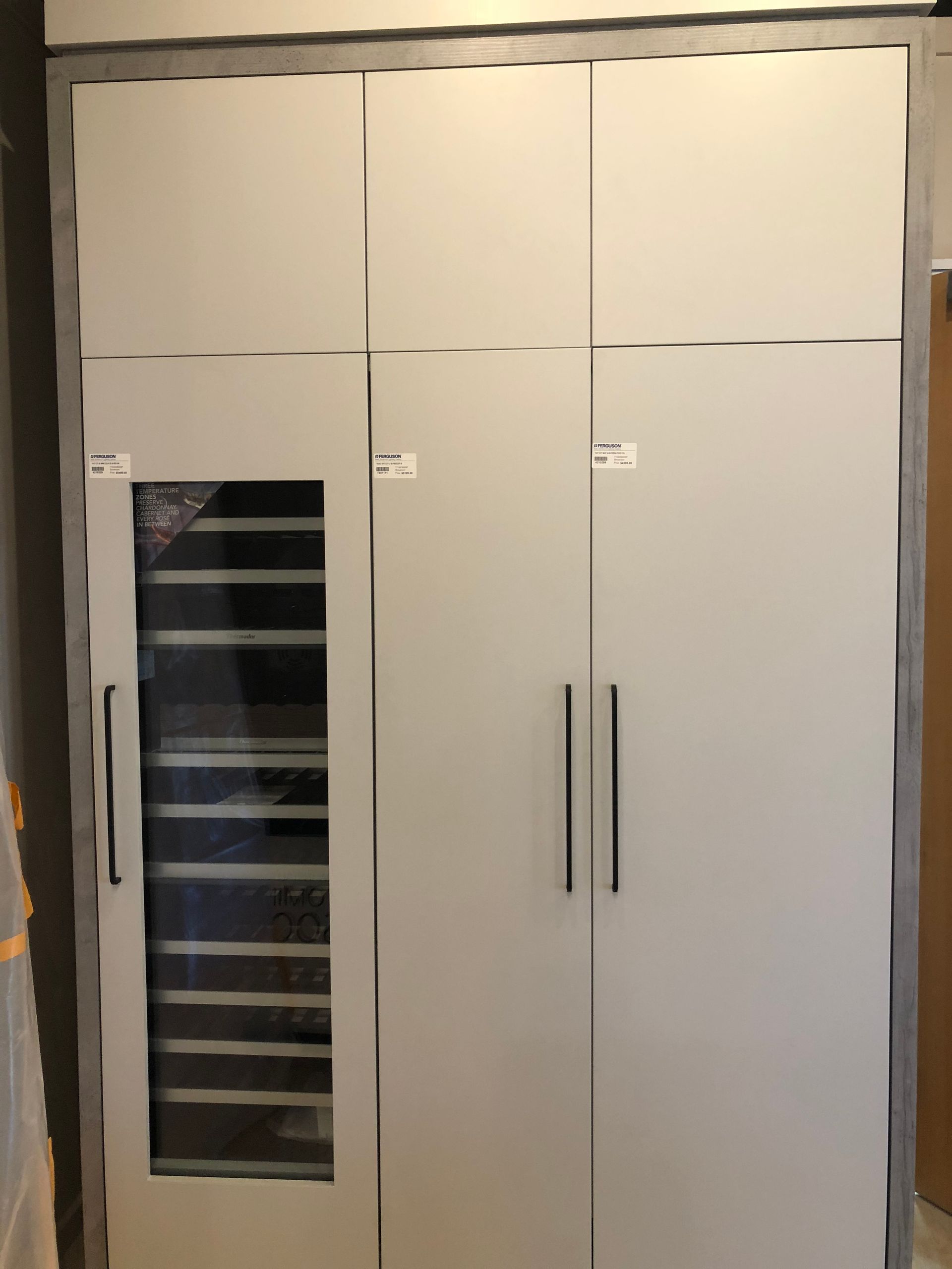 Tall, light gray wardrobe with three doors, one glass pane showing drawers. Black handles and trim.