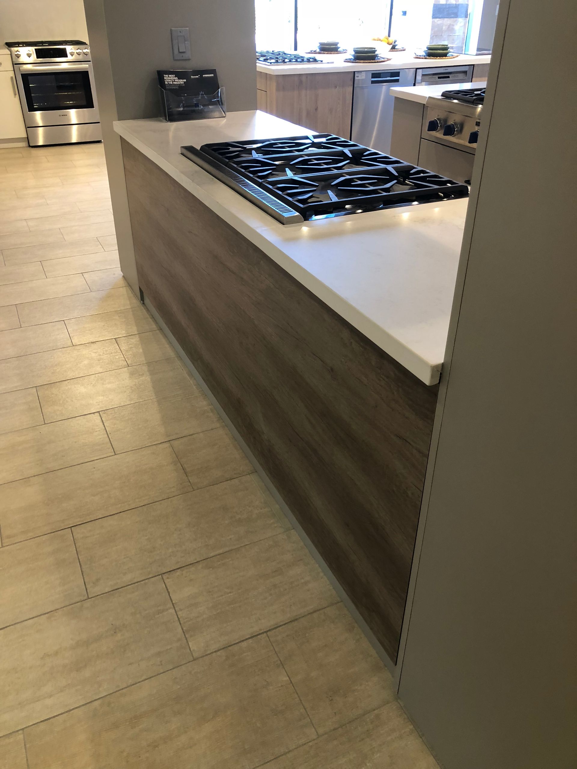 Kitchen island with cooktop, white countertop, and wood grain paneling.