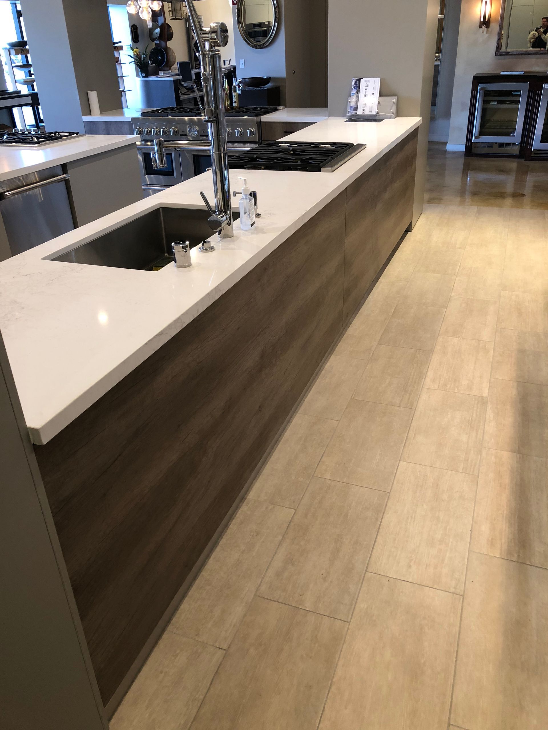 Modern kitchen island with white countertop and wood-grain paneling. Sink and stovetop are integrated.