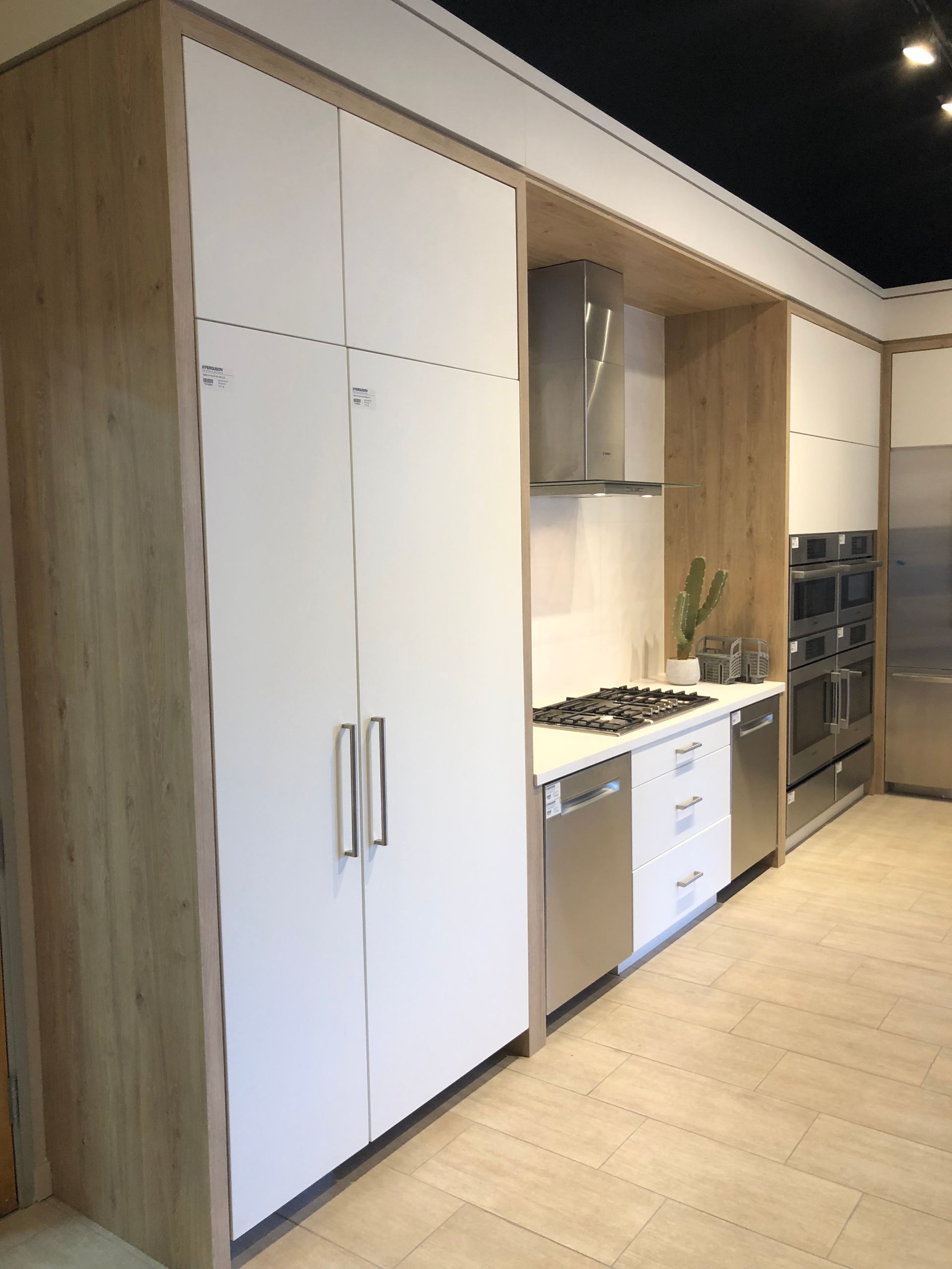 Modern kitchen with light wood cabinets, stainless steel appliances, and white doors.