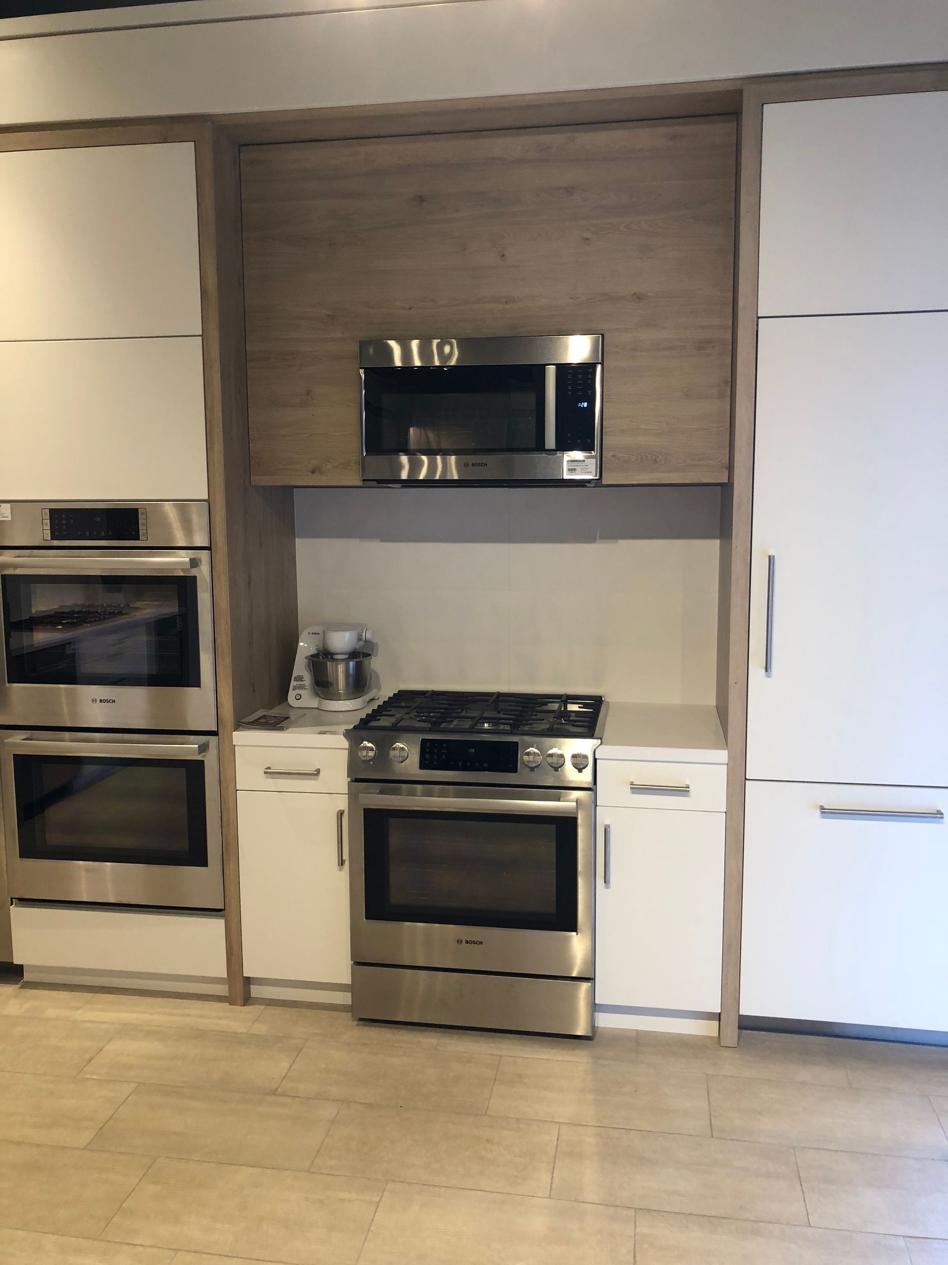 Modern kitchen with white and wood cabinetry, stainless steel appliances: oven, microwave, stovetop.