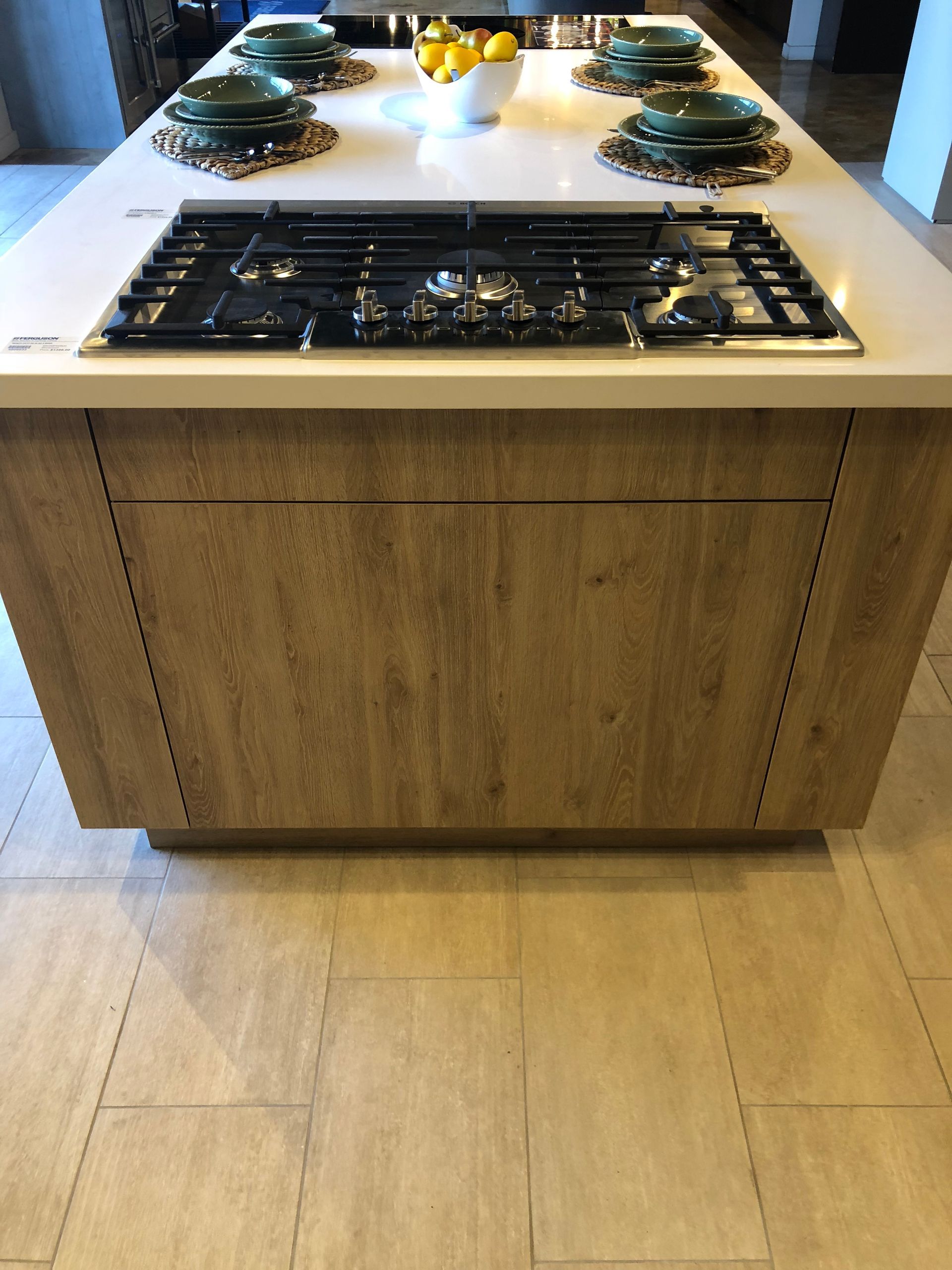 Kitchen island with stovetop, light wood cabinets, light countertop, and plates.