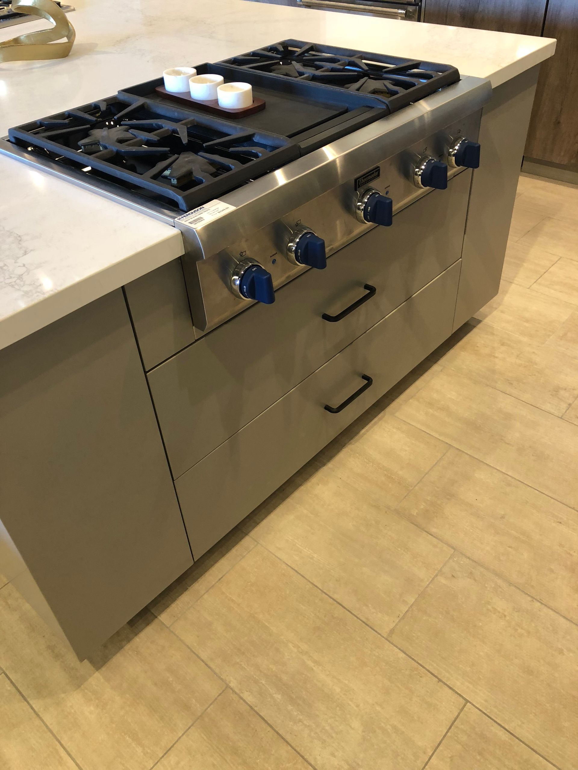Kitchen island with a gas cooktop and stainless steel appliances, with grey cabinetry and blue knobs.