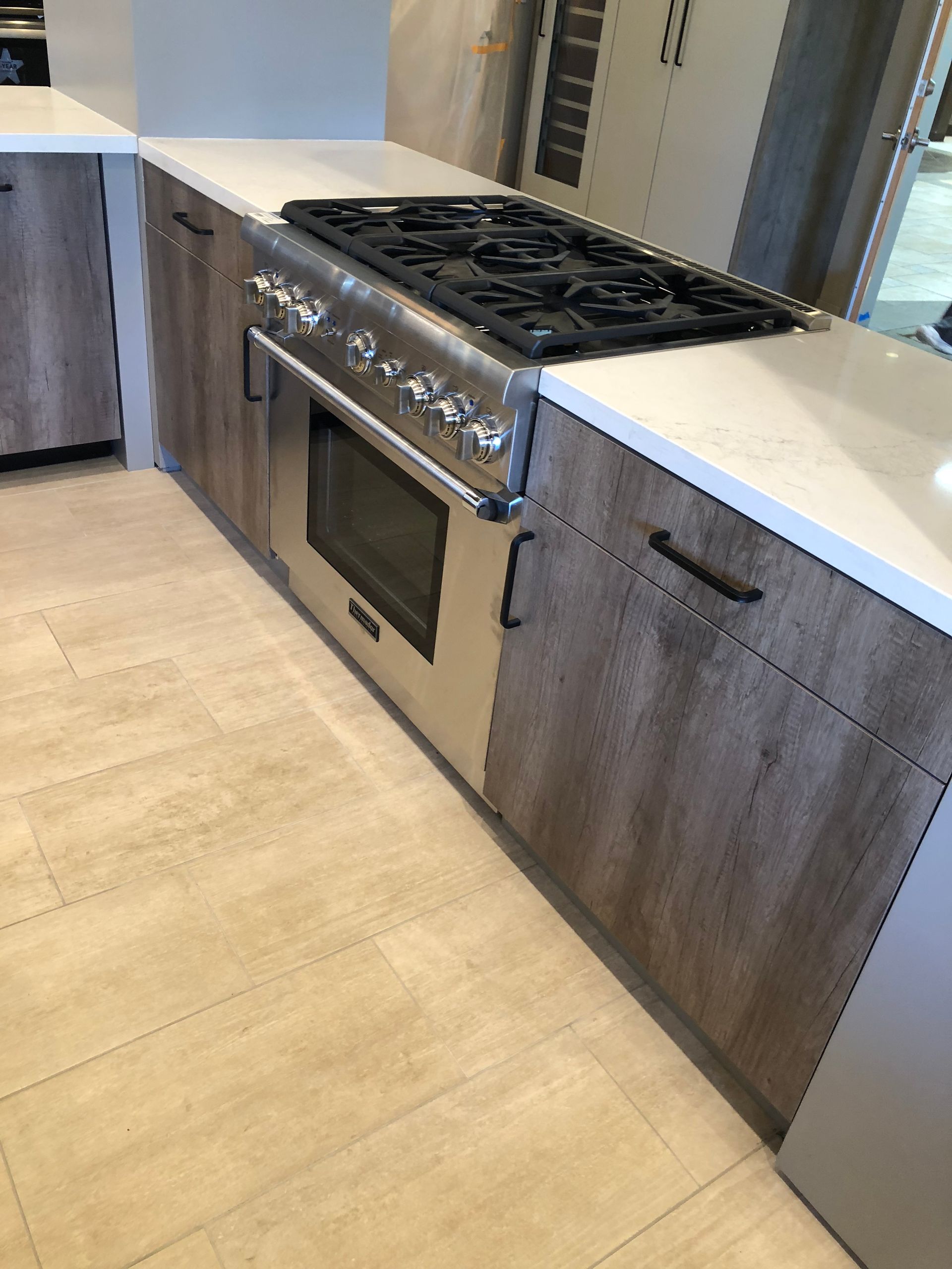 Kitchen with stainless steel oven and stovetop, light wood cabinets, white countertop, and light-colored flooring.