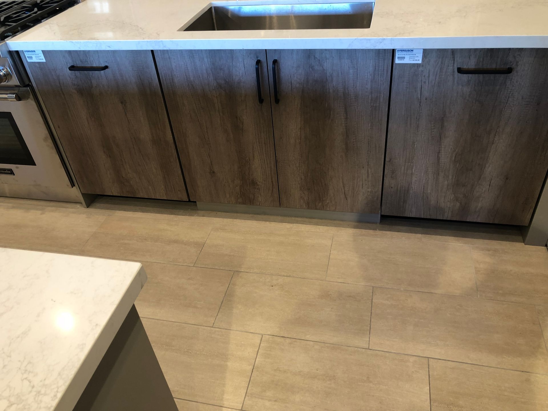 Kitchen island with wood-look cabinet doors, a light countertop, and beige tile flooring.