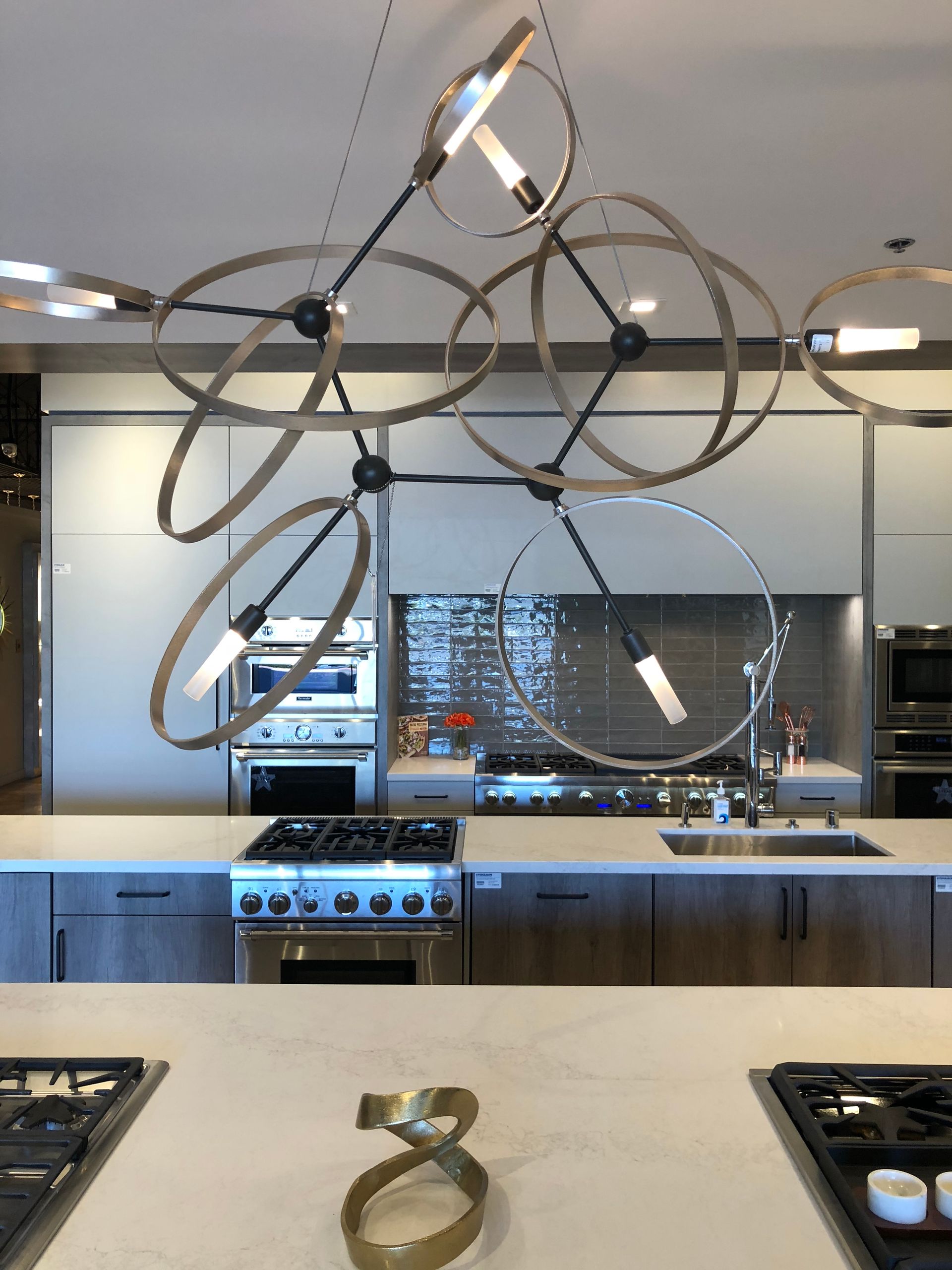 Modern kitchen with a geometric chandelier over a large island and stainless steel appliances.