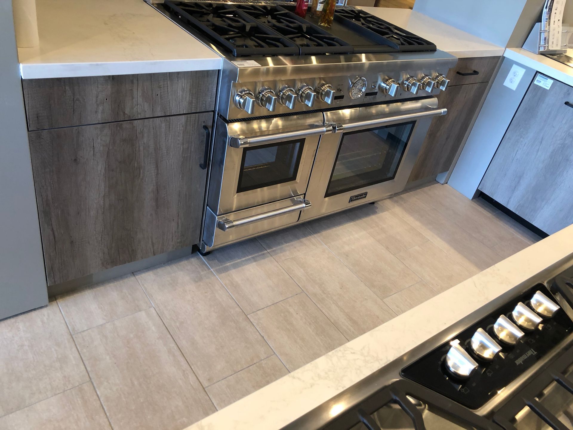 Stainless steel stove with double ovens in a modern kitchen, wooden cabinets, light tile floor.