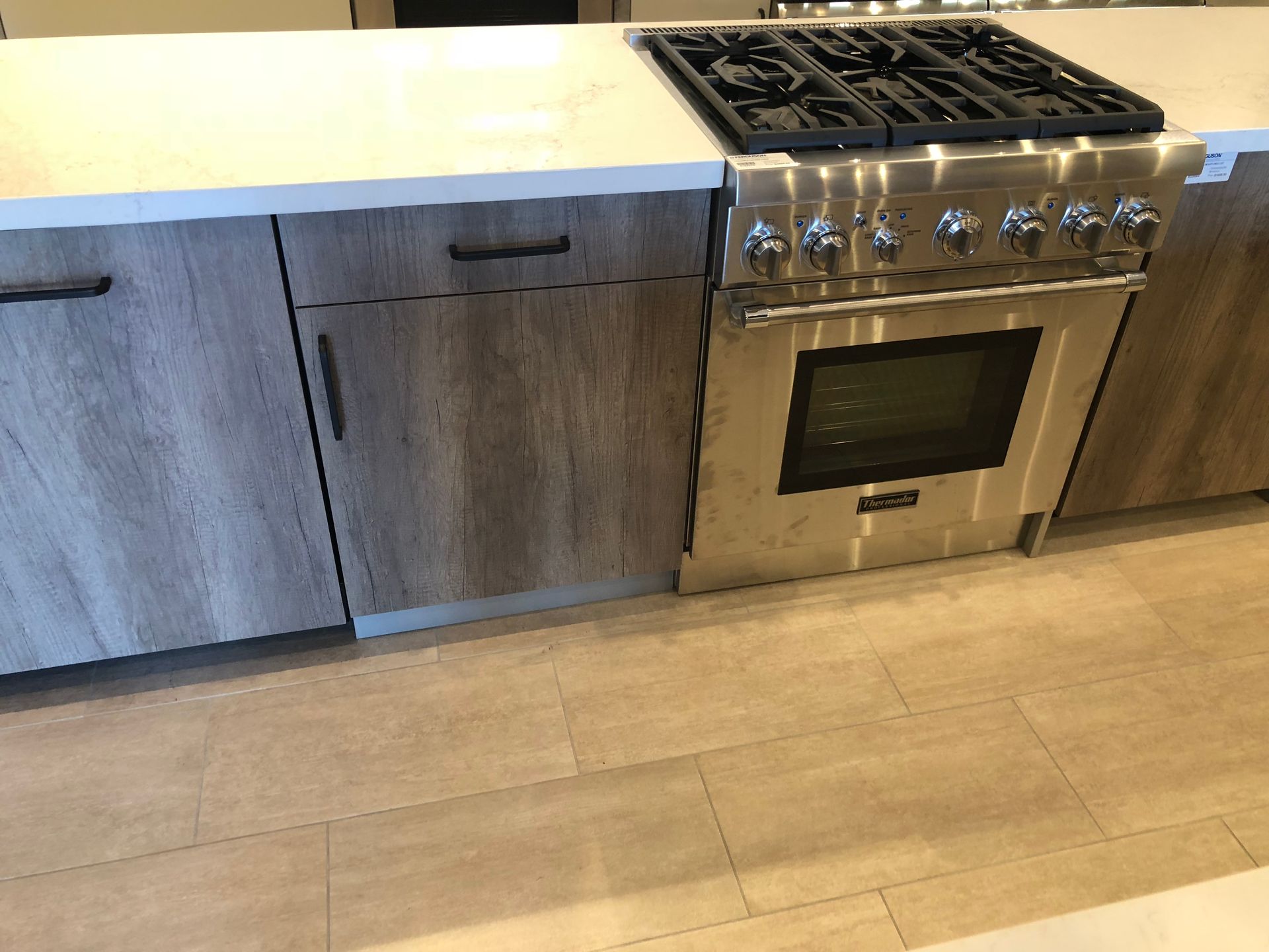 Kitchen with stainless steel oven and stovetop. Wood grain cabinets and light tile floor.