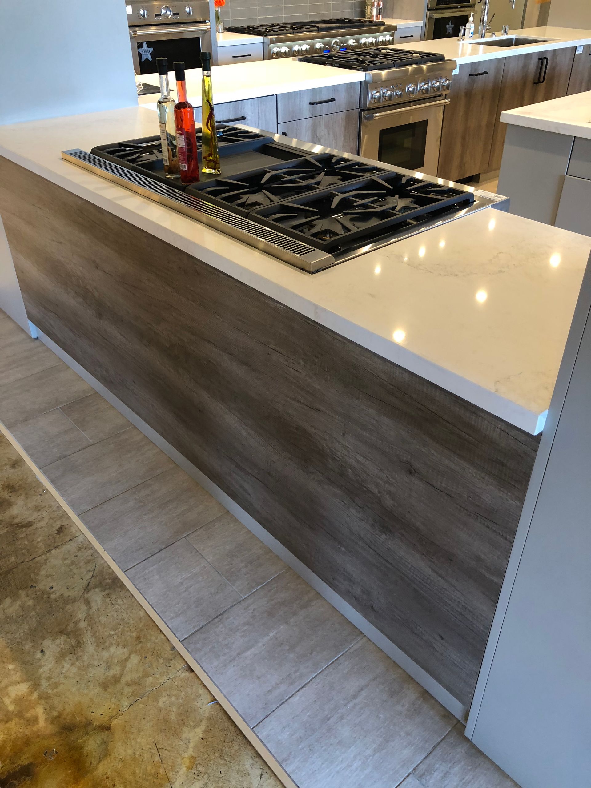 Kitchen island with a cooktop, light wood paneling, and white countertop.