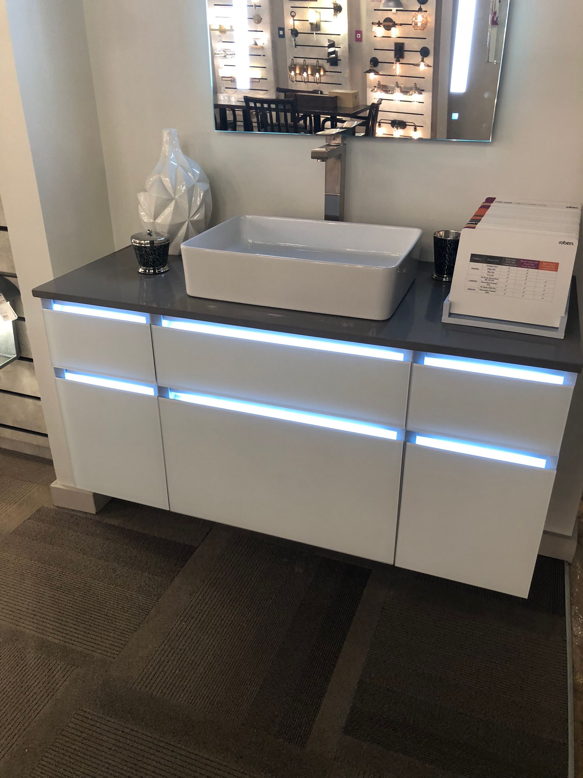 White bathroom vanity with glowing light strips, rectangular sink, and gray countertop.