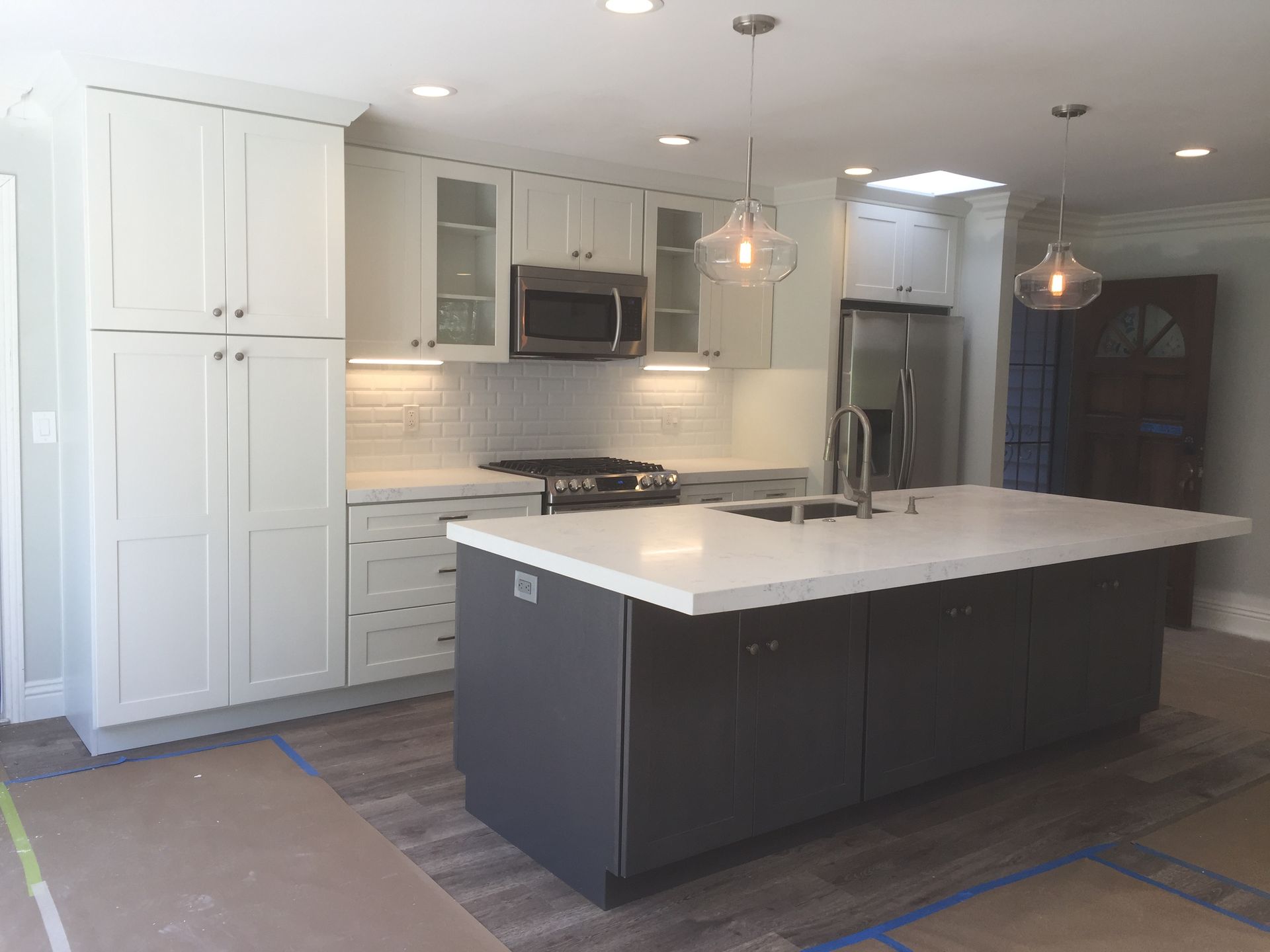 Modern kitchen with white cabinets, gray island, stainless steel appliances, and pendant lights.
