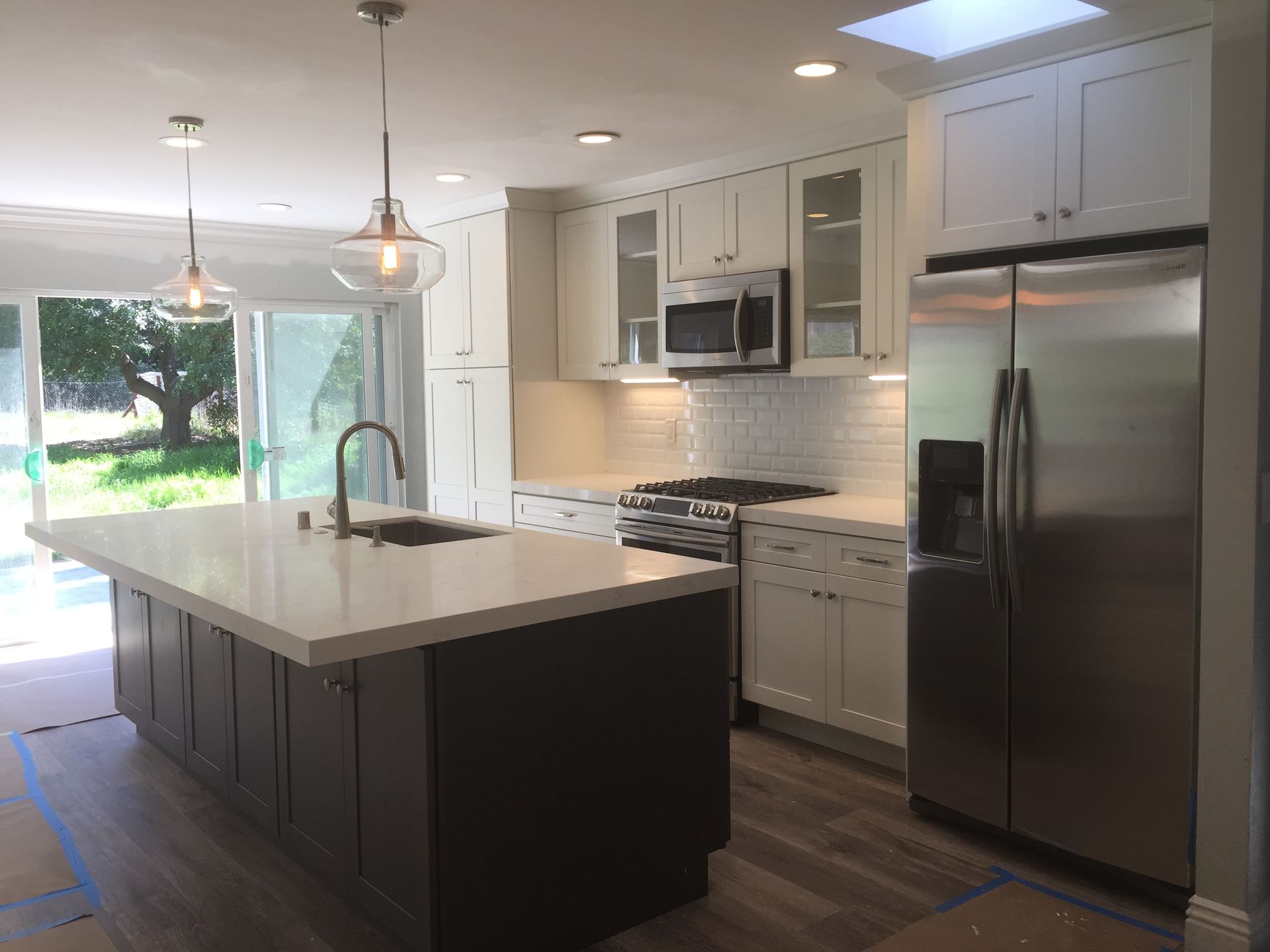 Modern kitchen with white cabinets, a dark island, stainless steel fridge, and large windows.