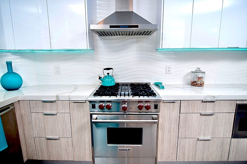Modern kitchen with stainless steel appliances and light wood cabinets. Turquoise accents, white countertops, and backsplash.