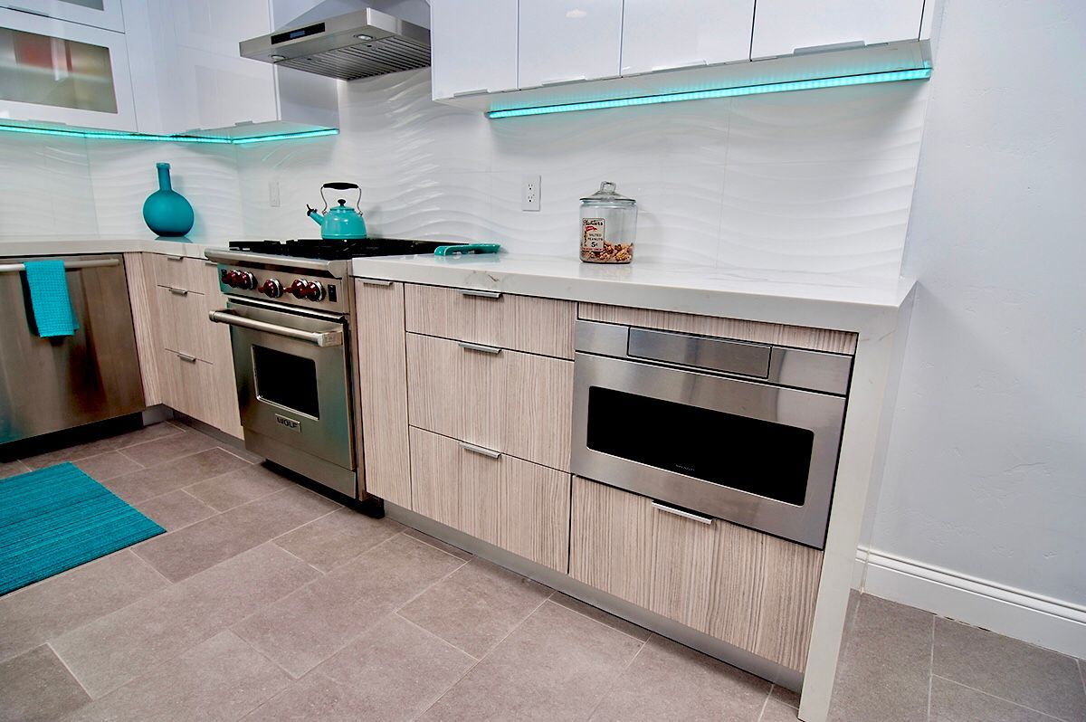 Modern kitchen with stainless steel appliances, light wood cabinets, white backsplash, and turquoise accents.