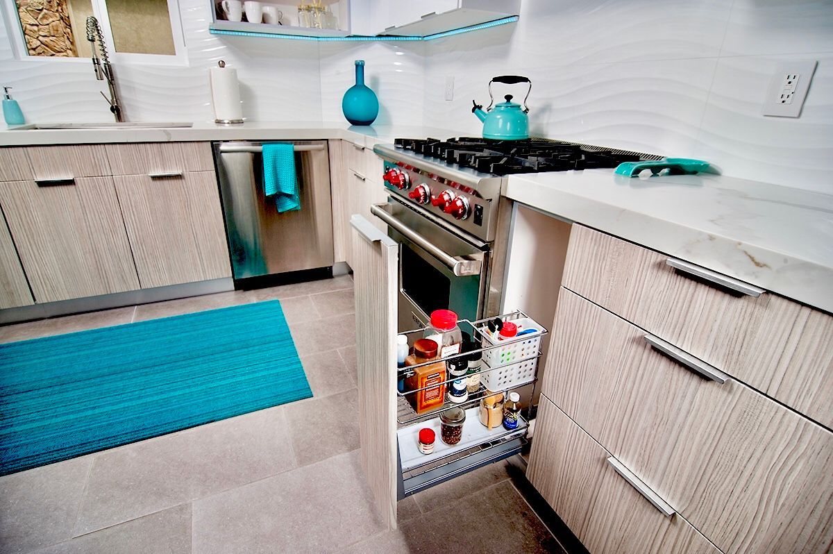 Modern kitchen with turquoise accents: gas range, spice rack, blue rug, light wood cabinets, and white countertops.