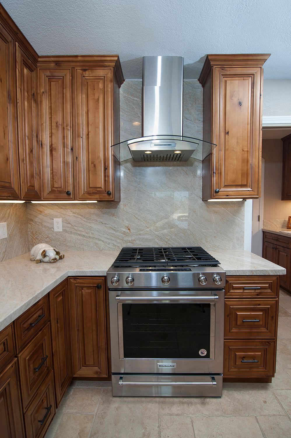 Kitchen with stainless steel range and hood, wood cabinets, light countertops, and tile backsplash.