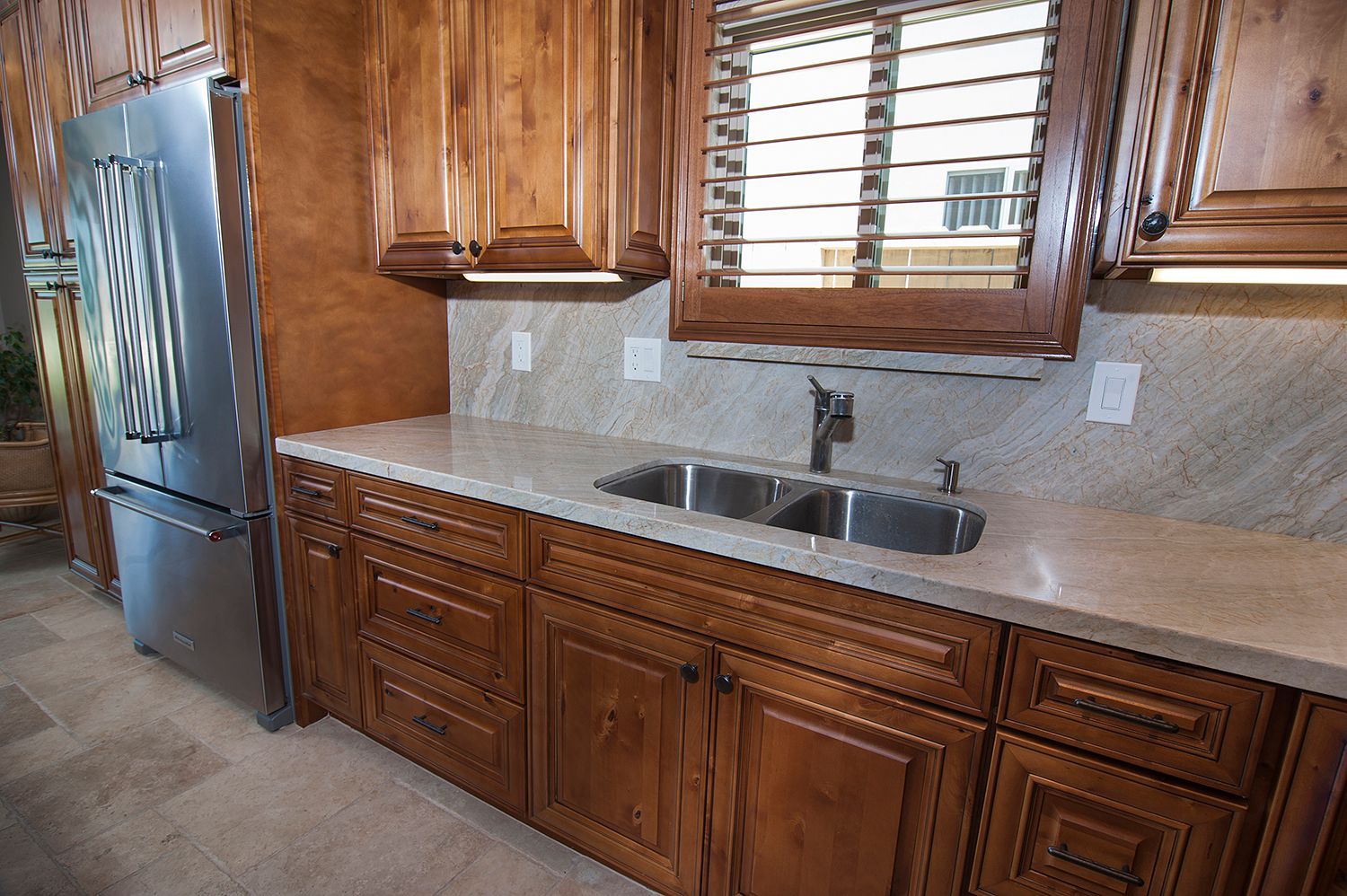 Kitchen with wooden cabinets, stainless steel fridge, and a double sink.