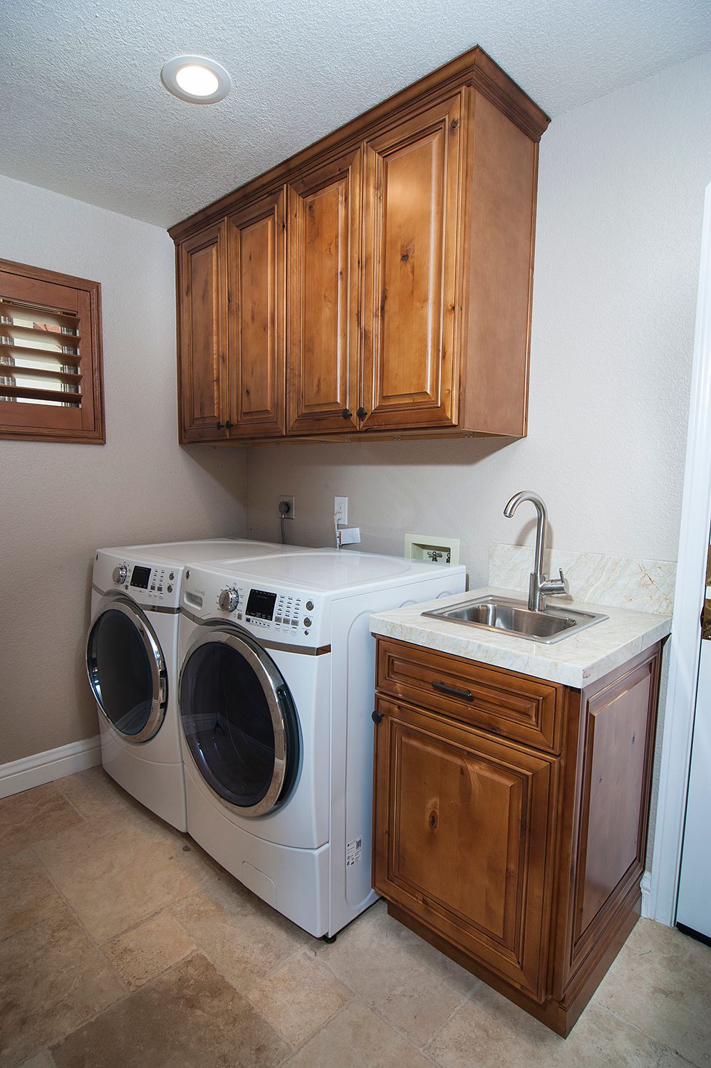 Laundry room with white machines, brown cabinets, and a small sink.