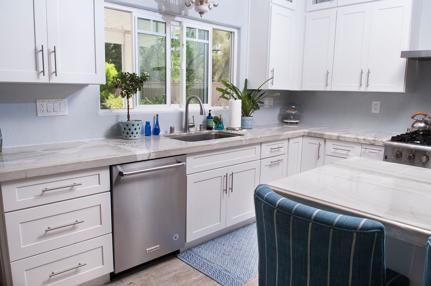 White kitchen with stainless steel appliances, blue and white accents, and a window overlooking greenery.