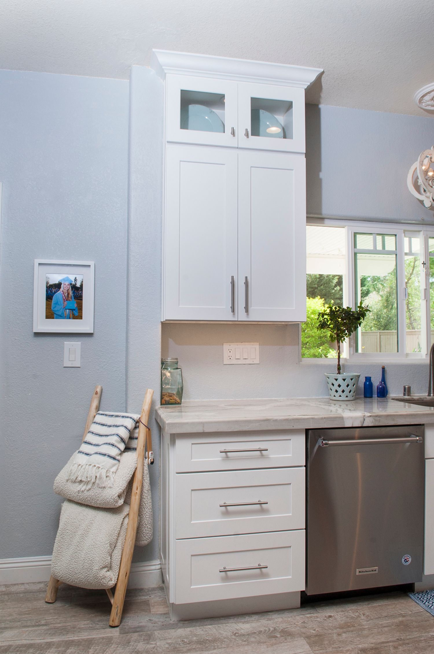 White kitchen cabinets with a dishwasher, countertop, and ladder holding pillows.