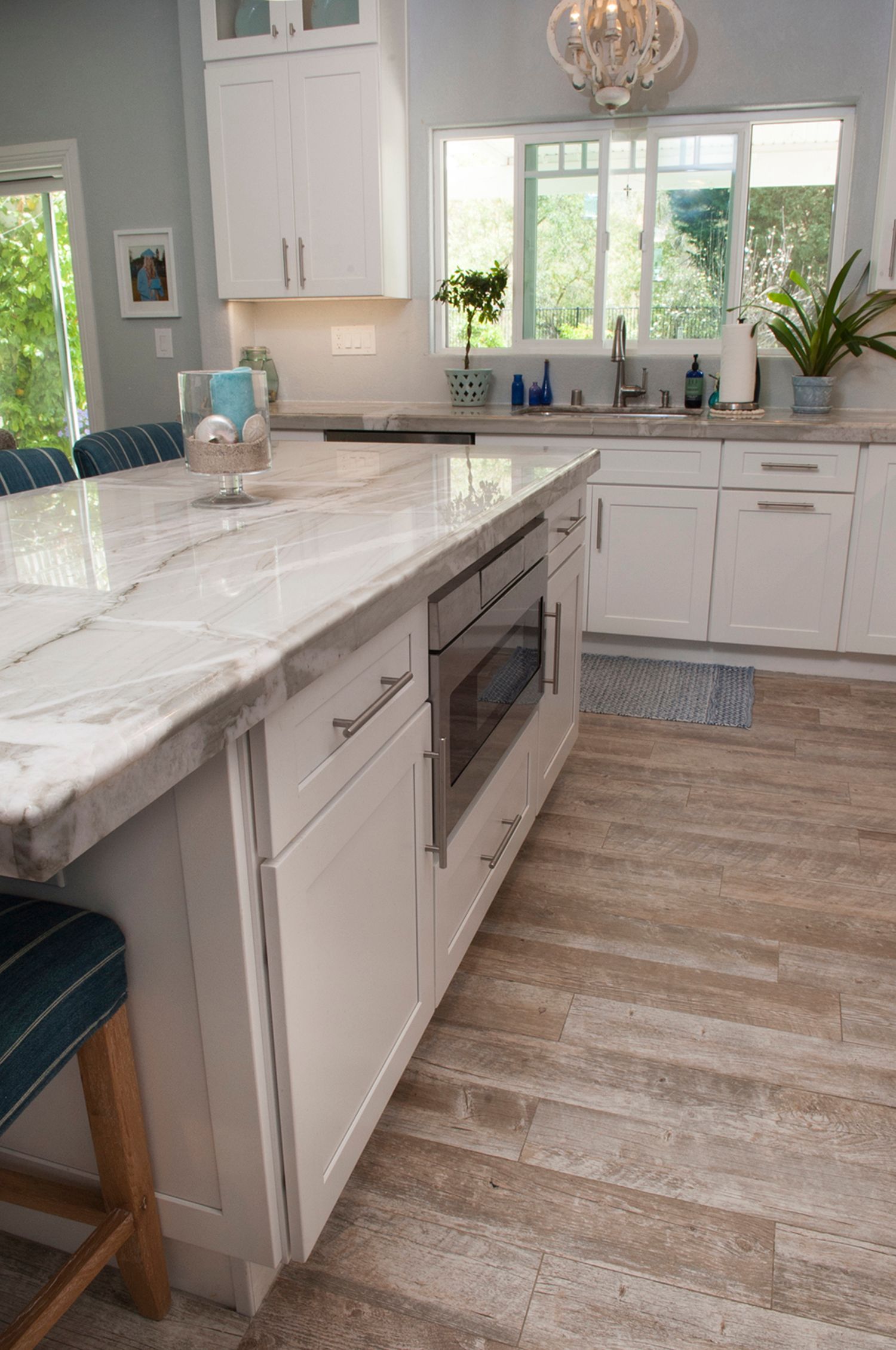 White kitchen with marble island, built-in microwave, wood-look floors, and natural light.