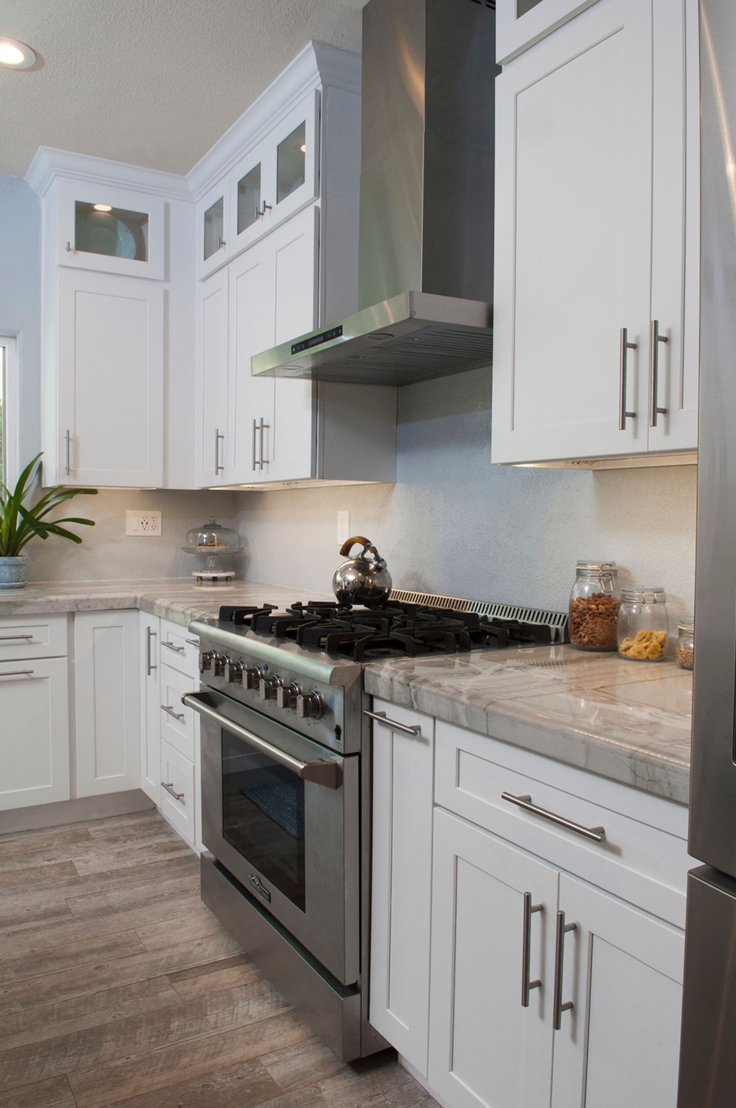 White kitchen with stainless steel appliances, stove, and range hood.