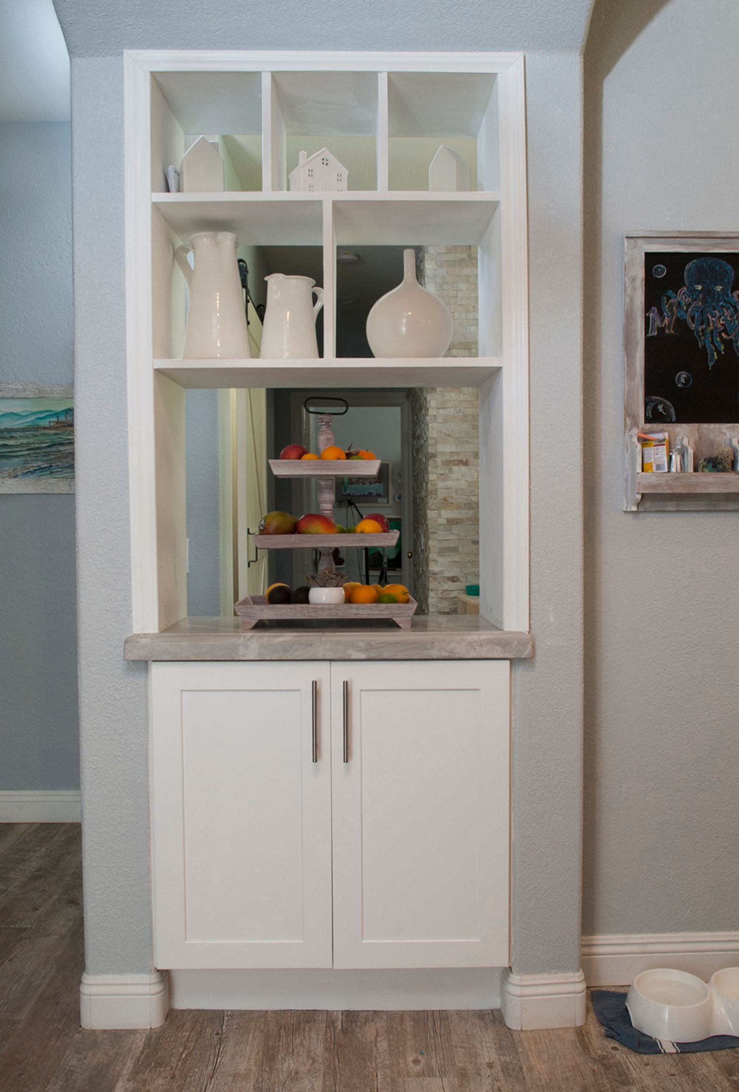 Built-in white cabinet with open shelves displaying decorative items, marble countertop, and mirrored back wall.