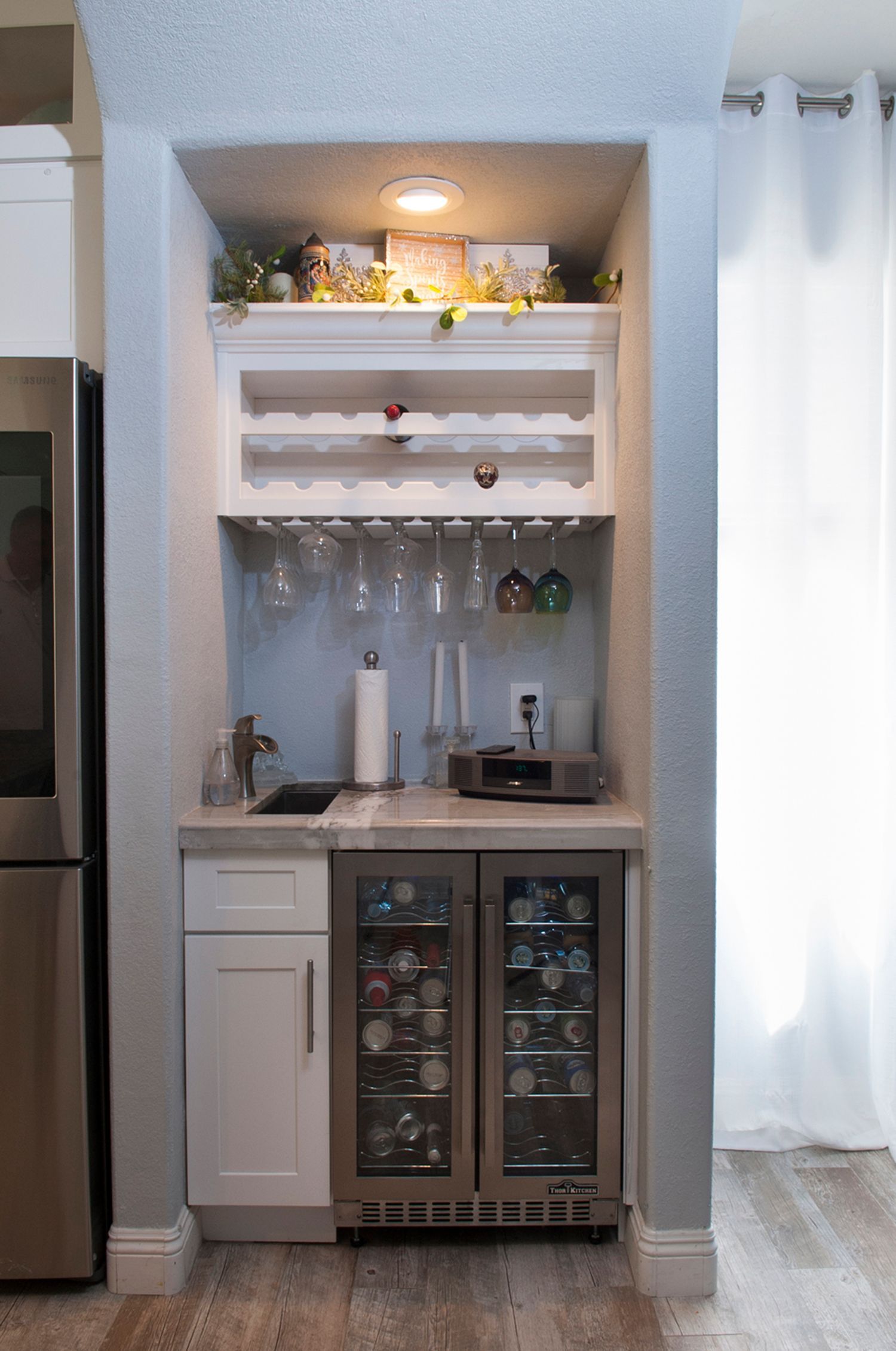 Built-in home bar with a wine fridge, sink, shelves, and glassware.