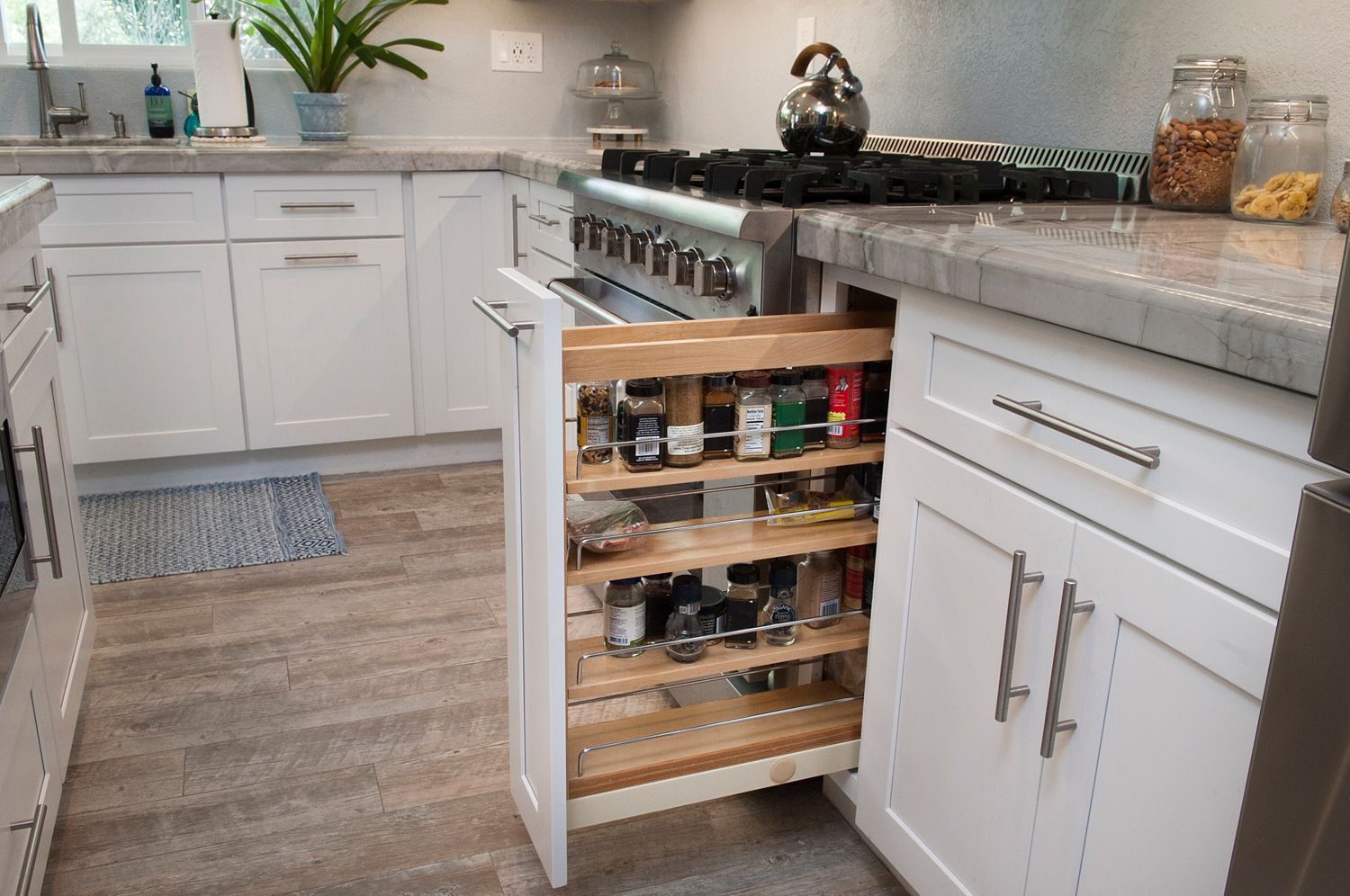 White kitchen with pull-out spice rack, gas range, and light-colored wood floor.