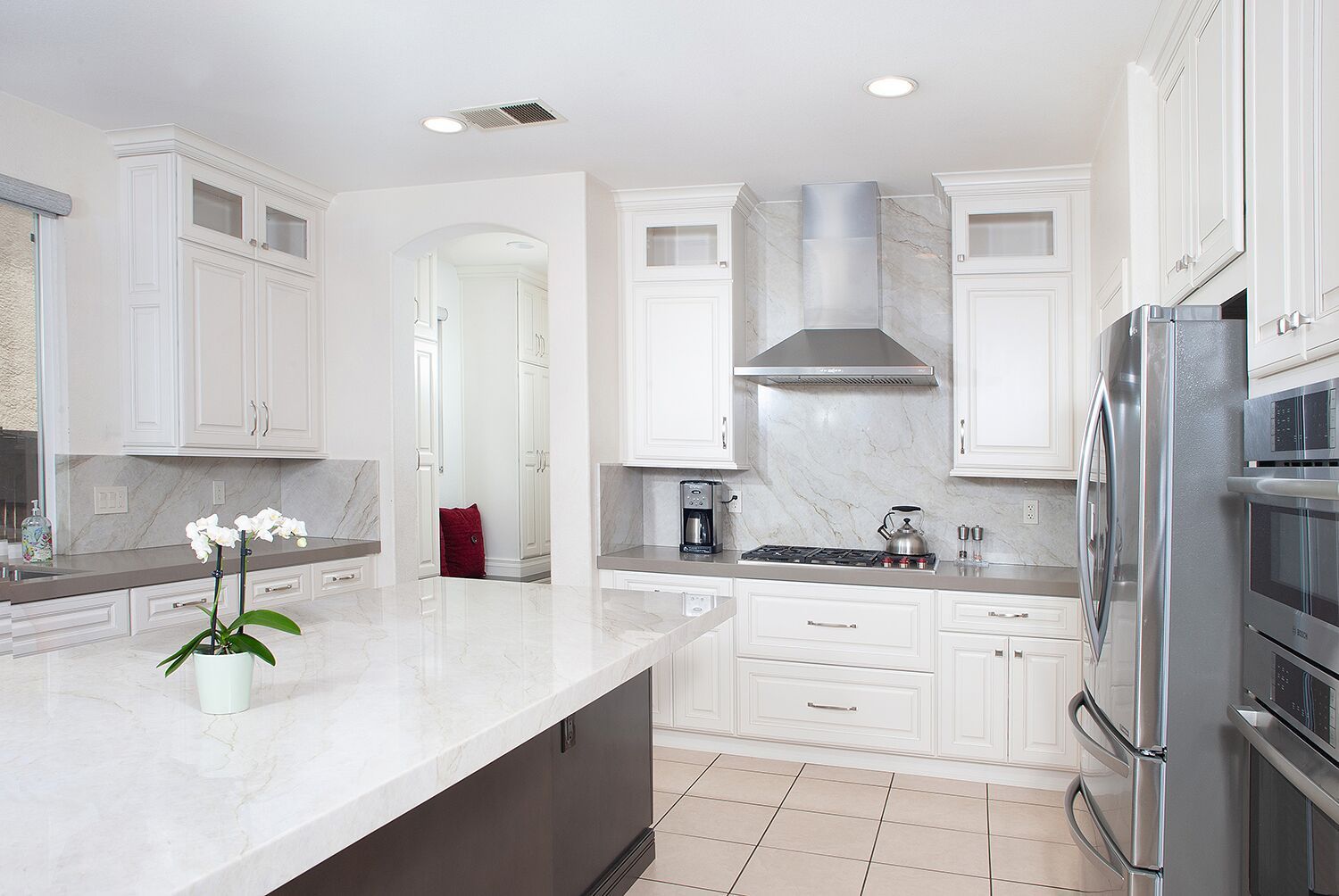 White kitchen with island, cabinets, appliances, and marble backsplash.