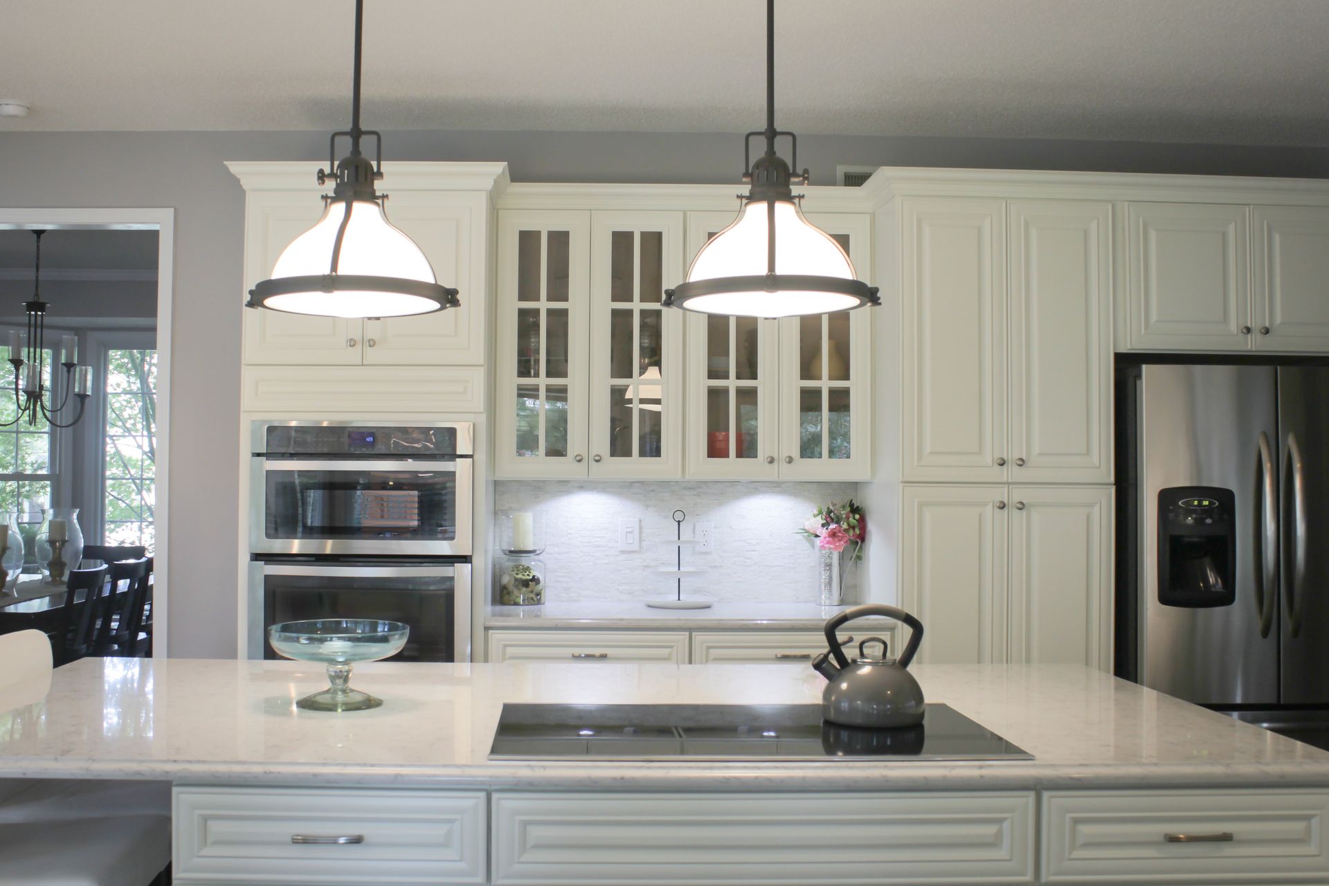 A white kitchen with a large island, overhead lights, and stainless steel appliances.
