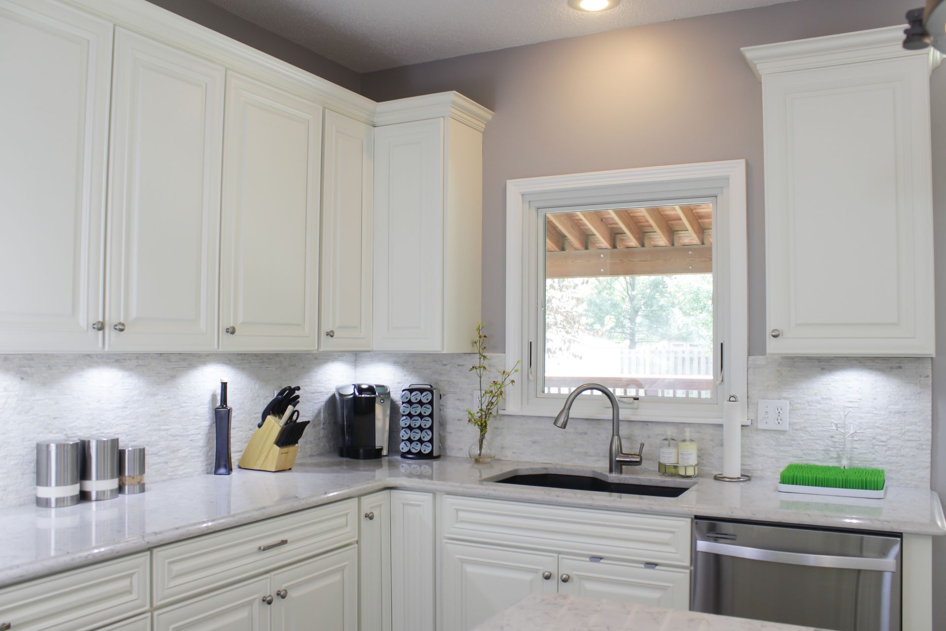 White kitchen with cabinets, countertop, sink, window, and appliances.
