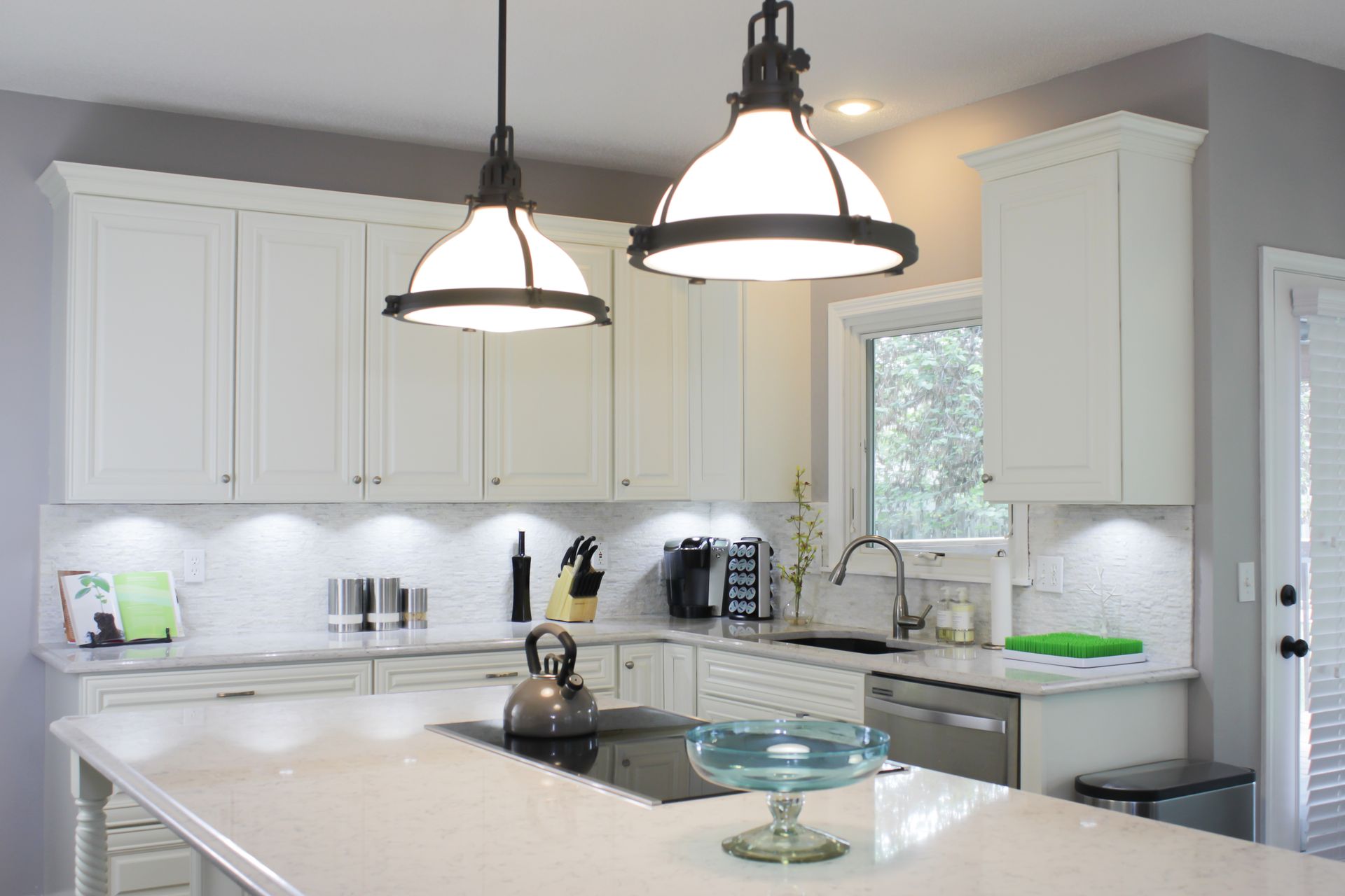 White kitchen with cabinets, island, pendant lights, and a window.