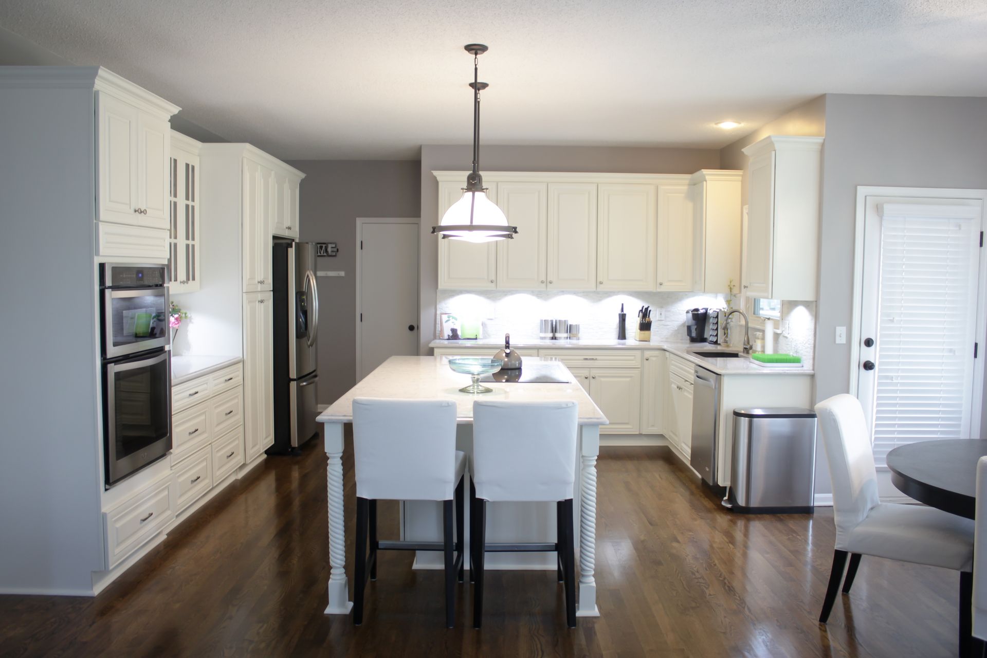White kitchen with island, cabinets, and stainless steel appliances on a hardwood floor.