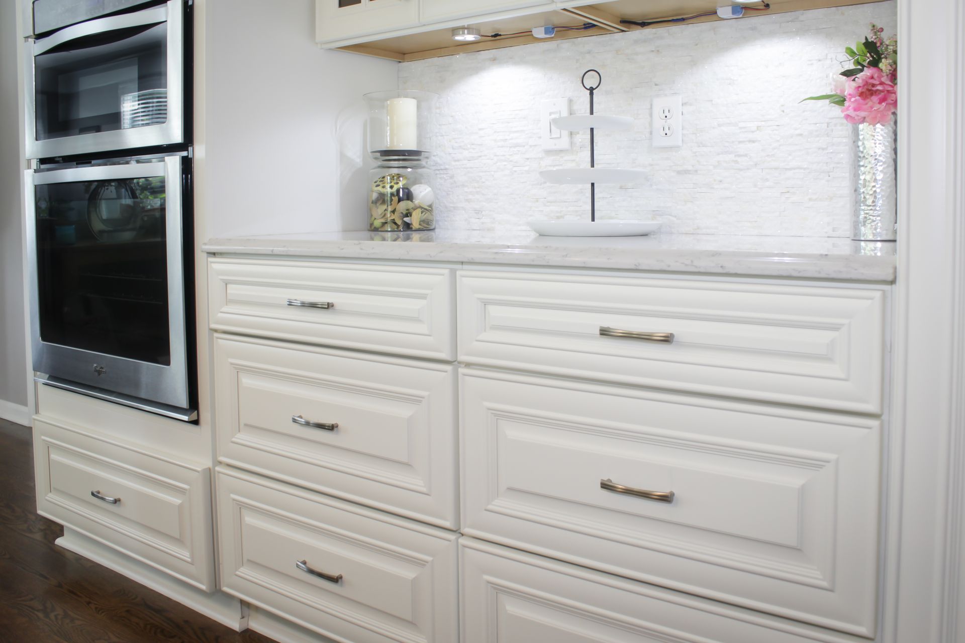White kitchen cabinets and built-in ovens, with a white backsplash, countertop, and decor.
