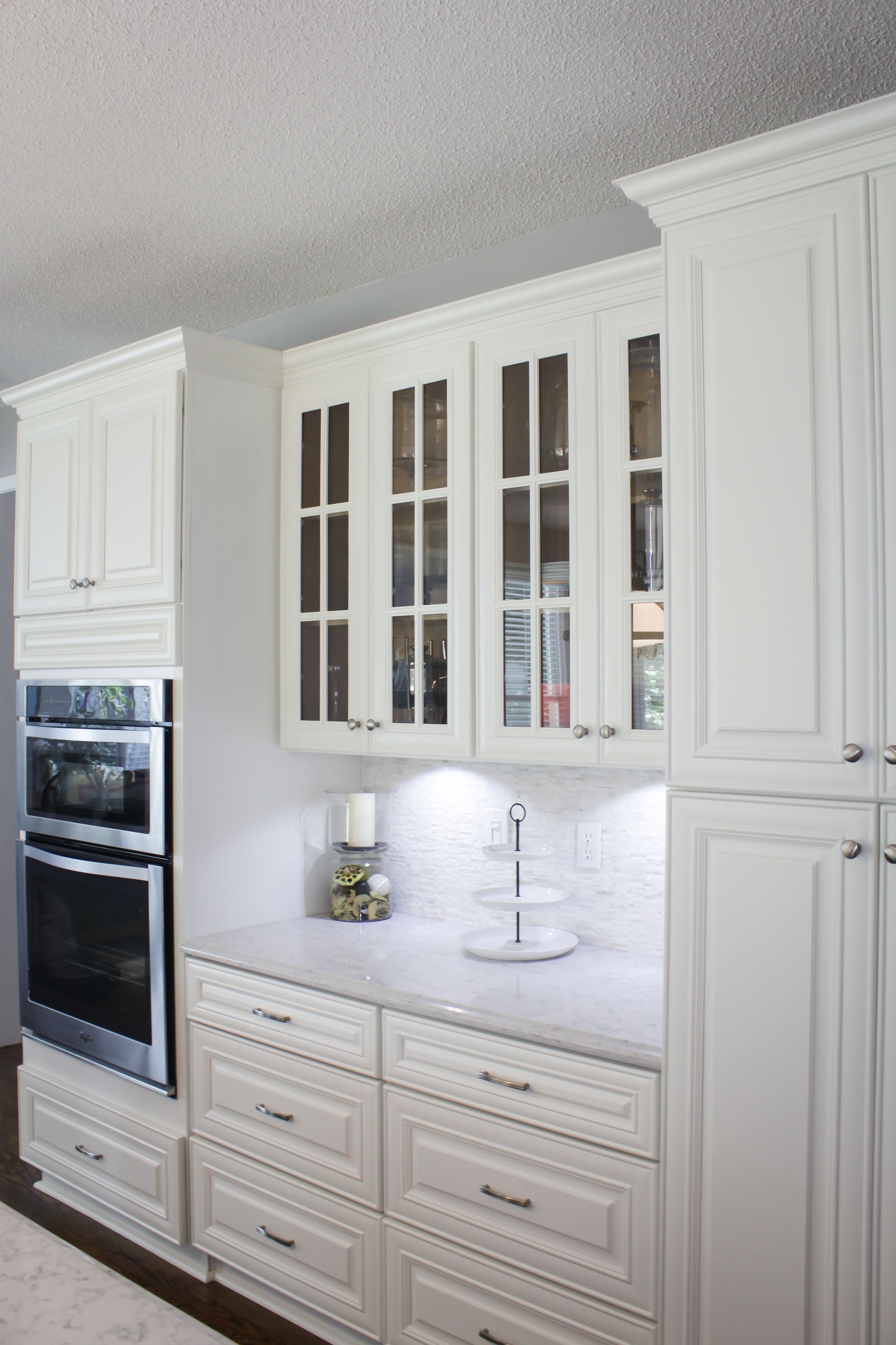 White kitchen cabinets with built-in oven, glass-front uppers, and a white countertop with drawers.