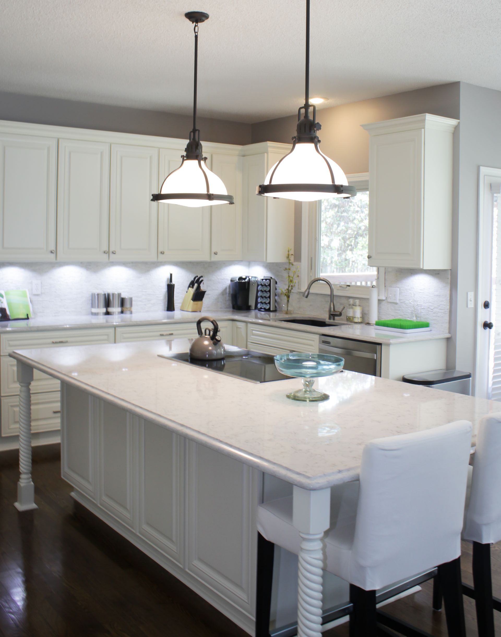 White kitchen with a large island, pendant lights, and white cabinets.