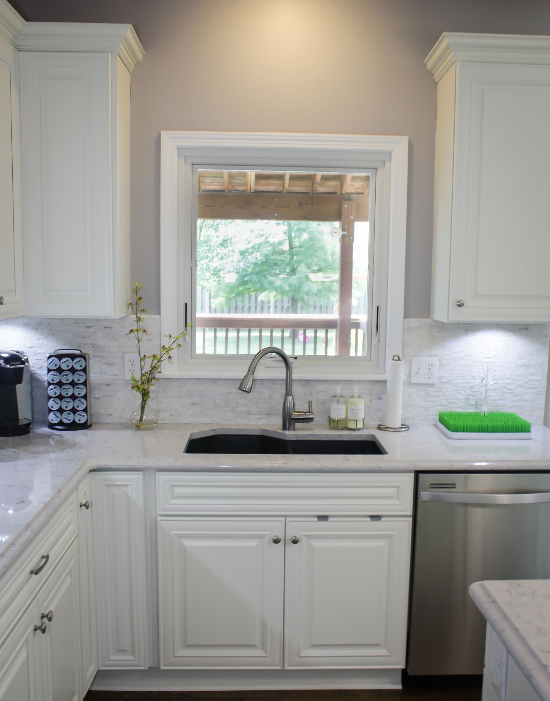White kitchen with cabinets, sink, window, and view of trees.