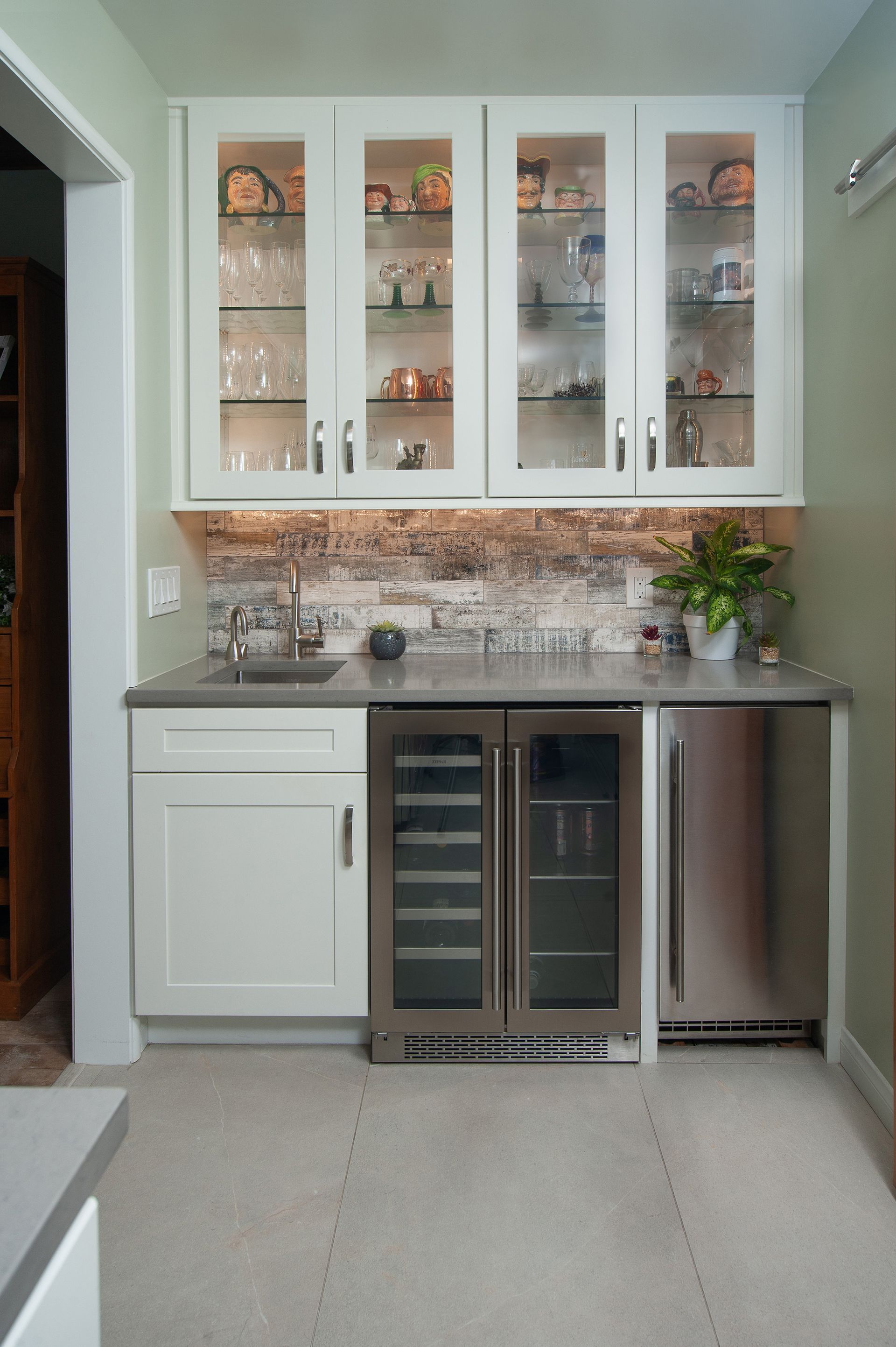 White built-in bar with glass cabinets, sink, wine fridge, and stainless steel refrigerator.