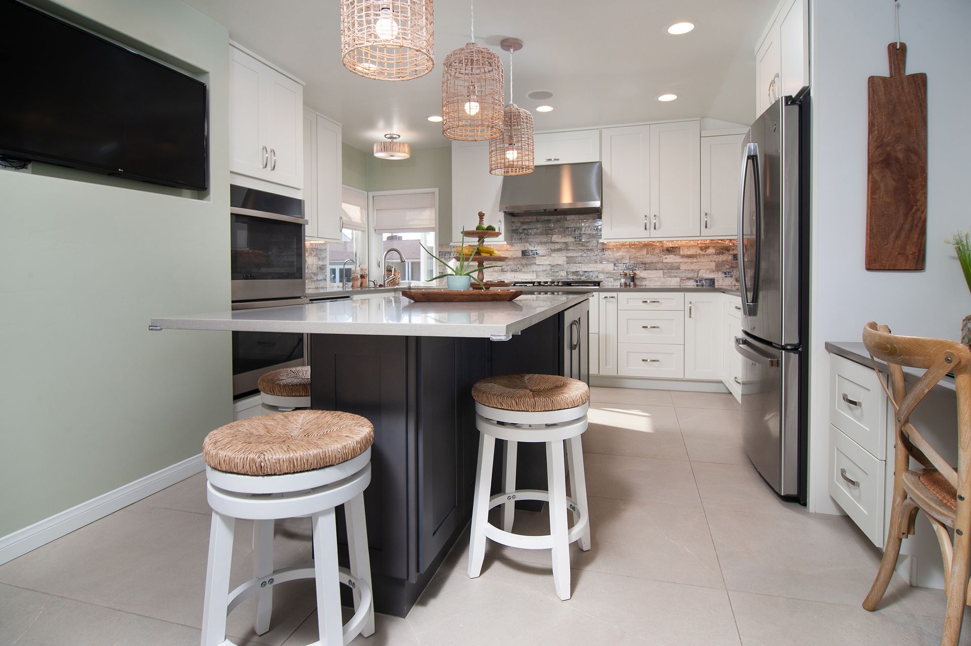 Modern kitchen with island, white cabinets, and three woven pendant lights. Two bar stools in foreground.