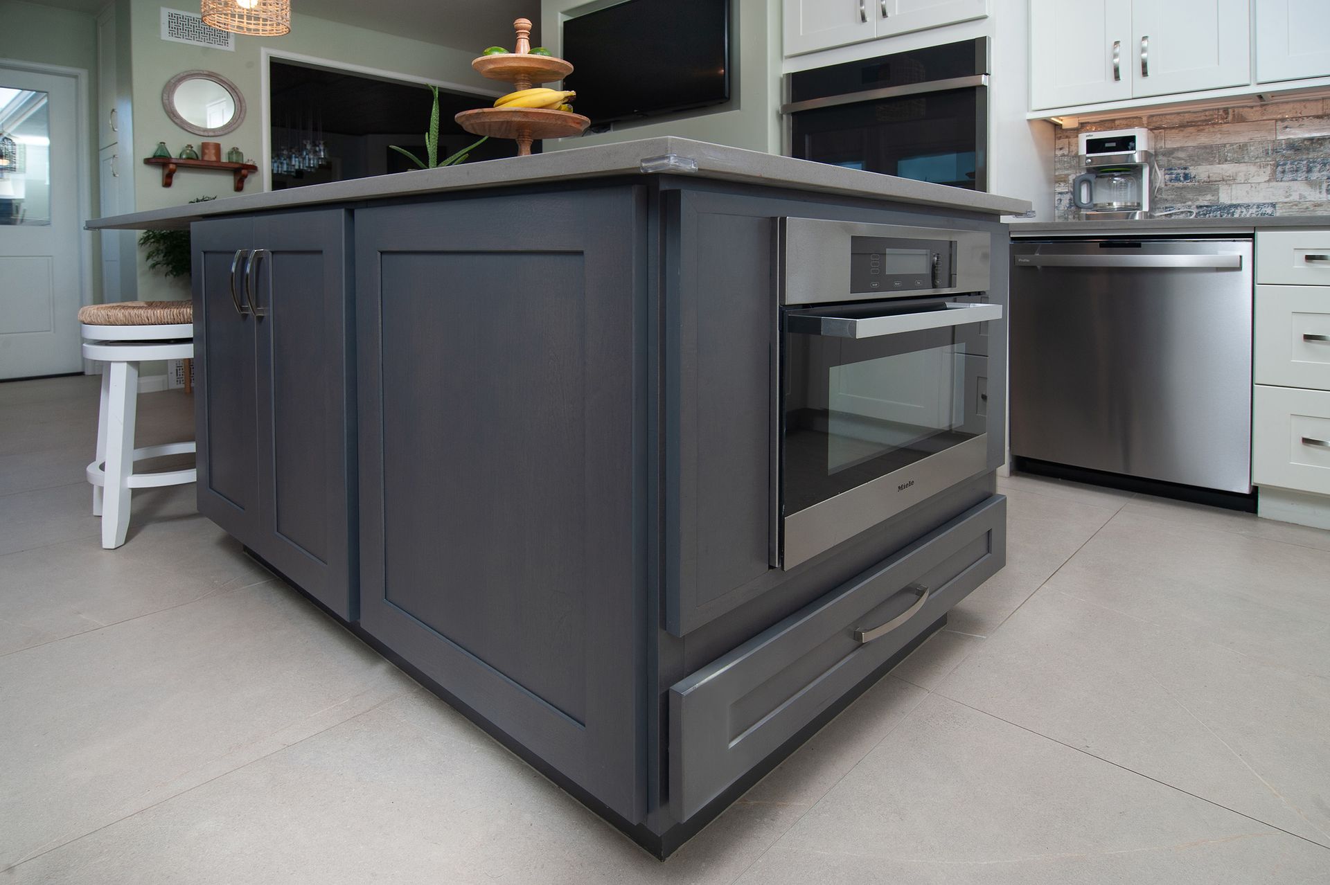 Gray kitchen island with a built-in oven and drawer. White cabinets and appliances surround it.
