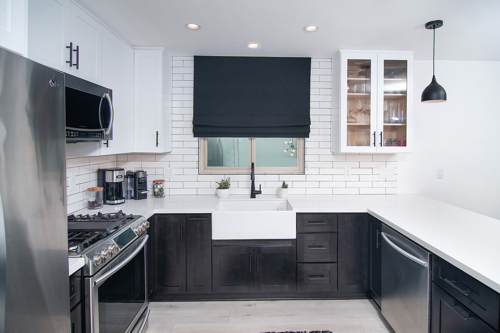 Modern kitchen with white counters, black and white cabinets, stainless steel appliances, and a farmhouse sink.