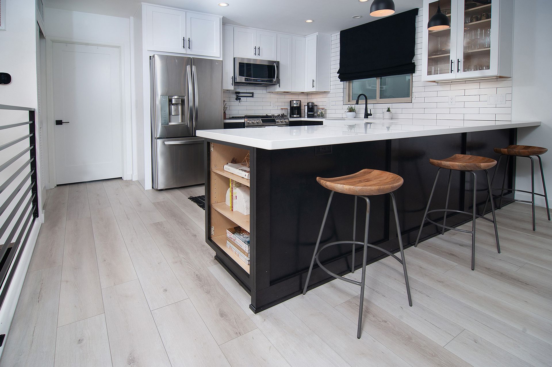Modern kitchen with white cabinets, black island, wooden stools, and light wood flooring.