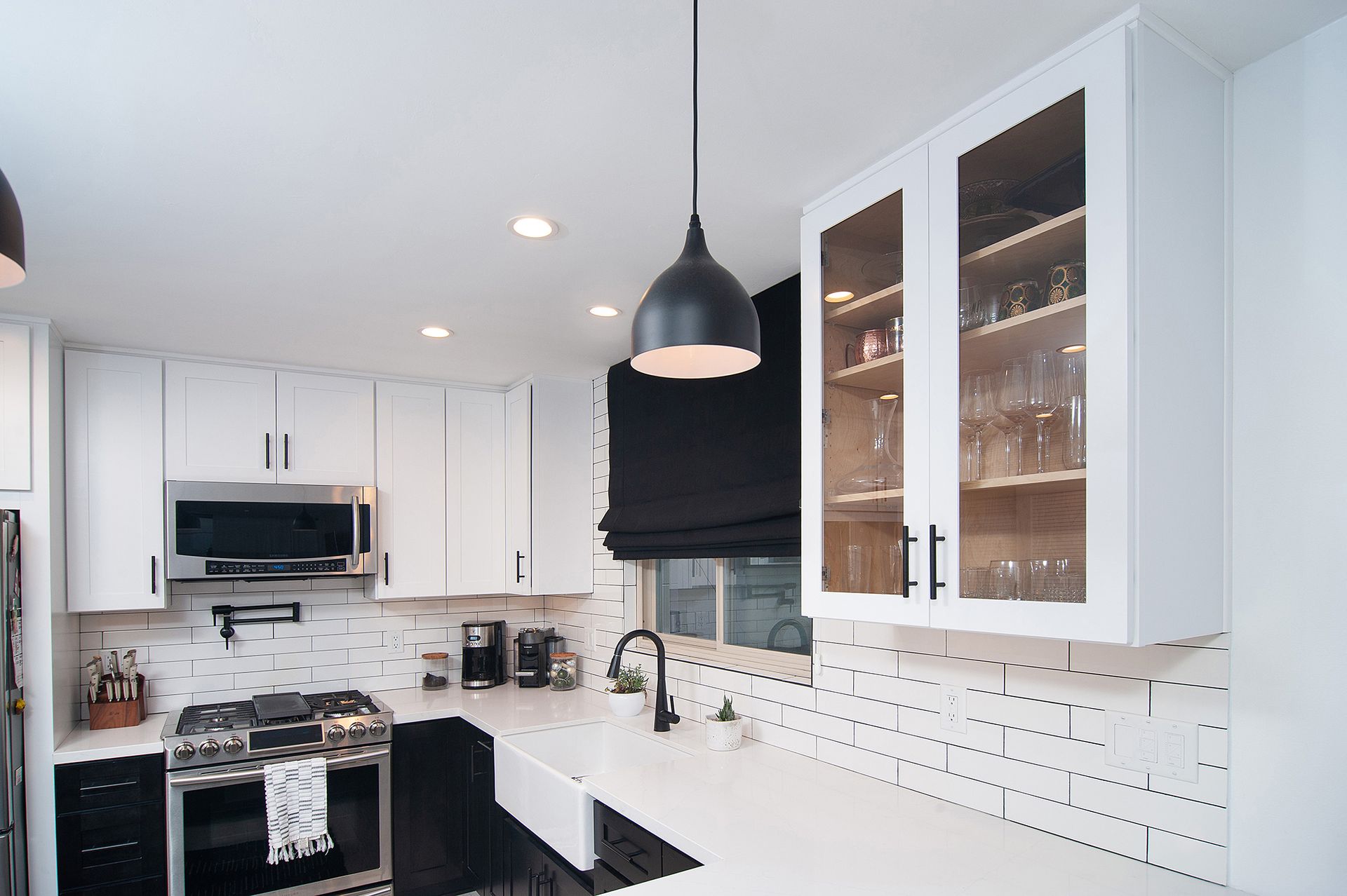 White kitchen with black accents, including cabinets, sink, and light fixtures; glass-front cabinet.