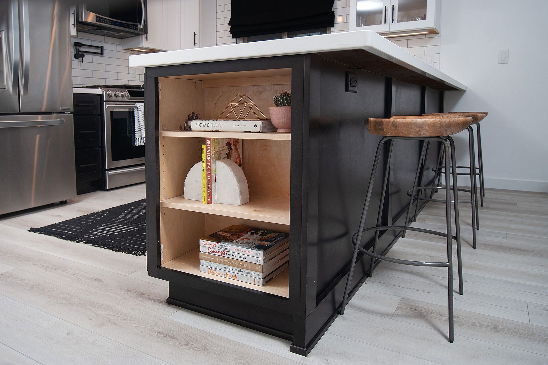 Black kitchen island with wooden shelves, white countertop, and two stools.